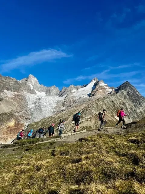 hikers ascending tour du mont blanc trail with alps peaks behind