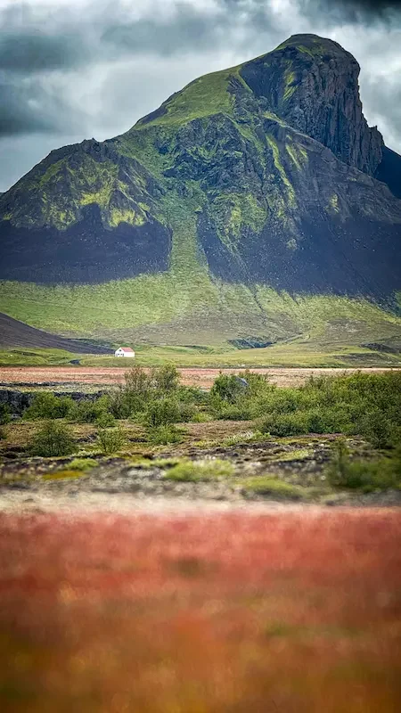 green mountain with black rock and small white building in front in iceland