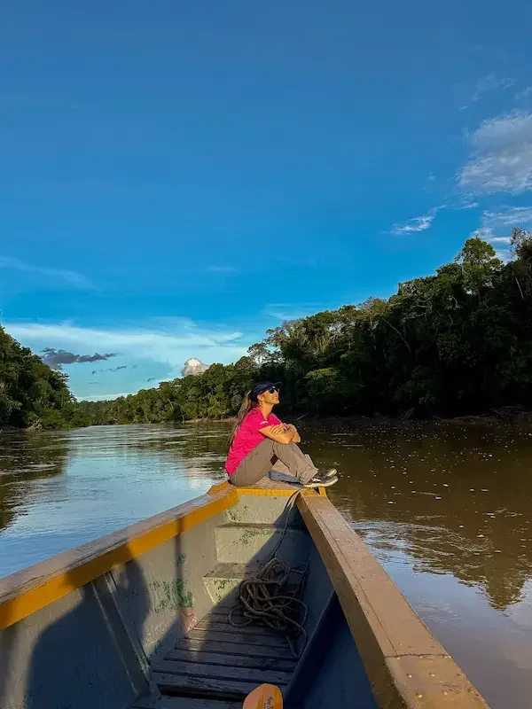 woman in pink shirt sitting on front of boat while on amazon river with rainforest on shoreline