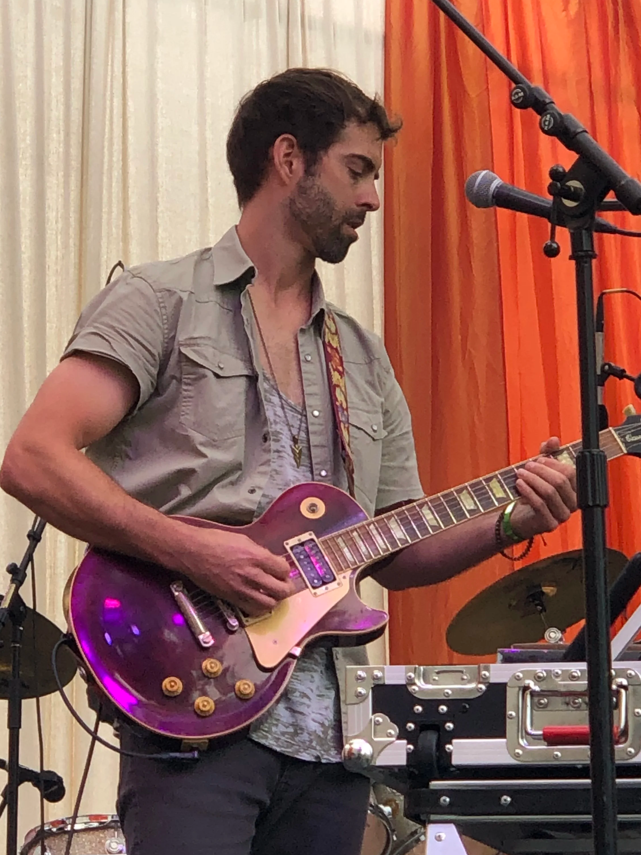 A man playing an electric guitar on stage, with a microphone and music equipment around him.