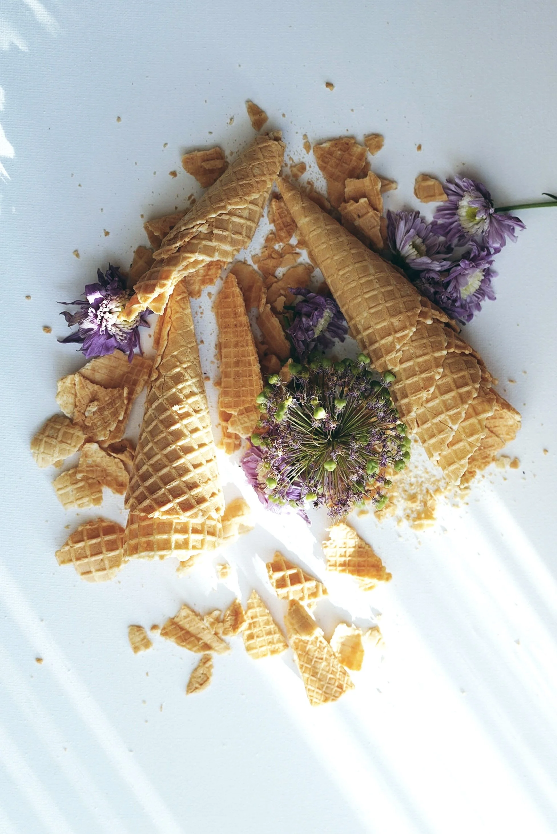 Broken ice cream cones with purple flowers on a white surface.
