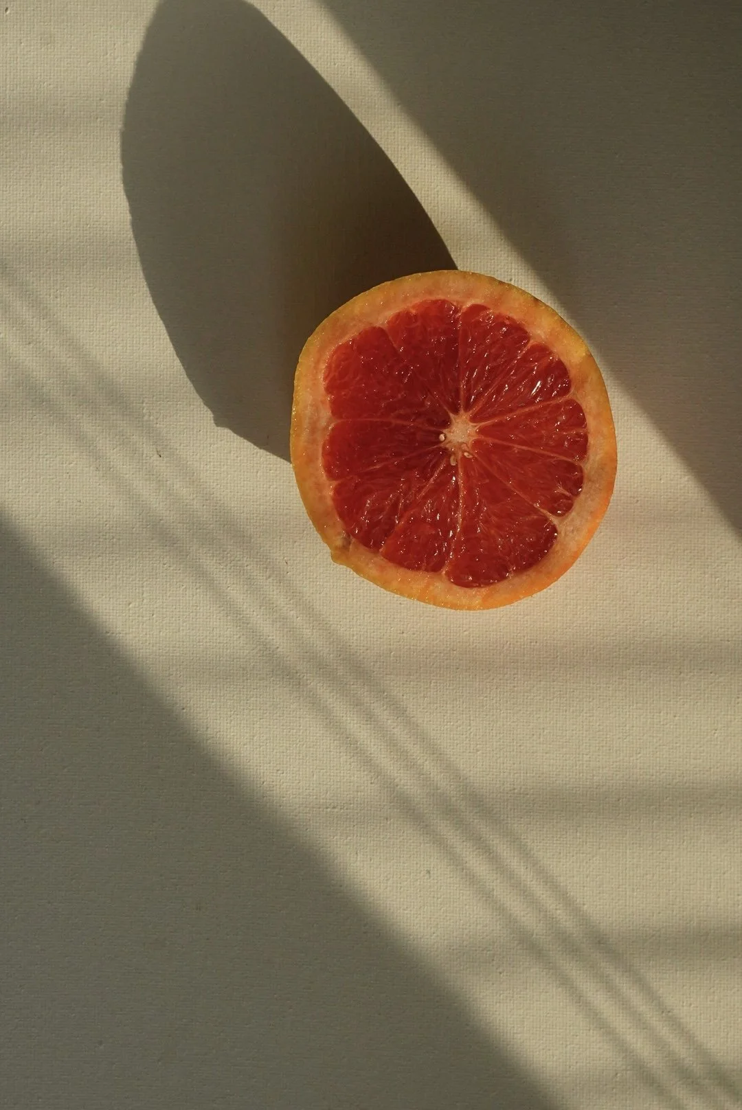 Half of a grapefruit on a white surface with shadows.