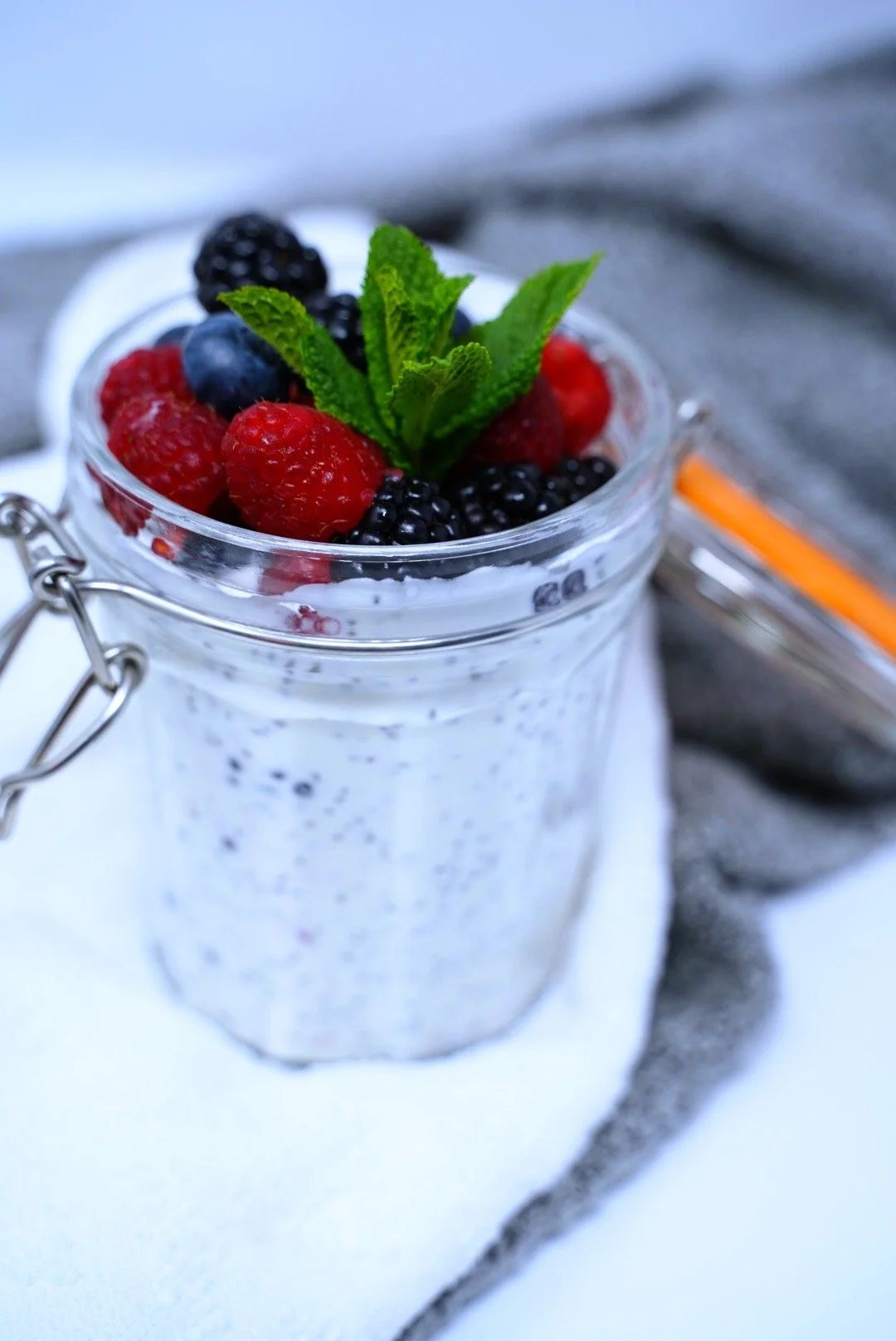 Jar filled with creamy dessert topped with fresh raspberries, blackberries, blueberries, and a sprig of mint.