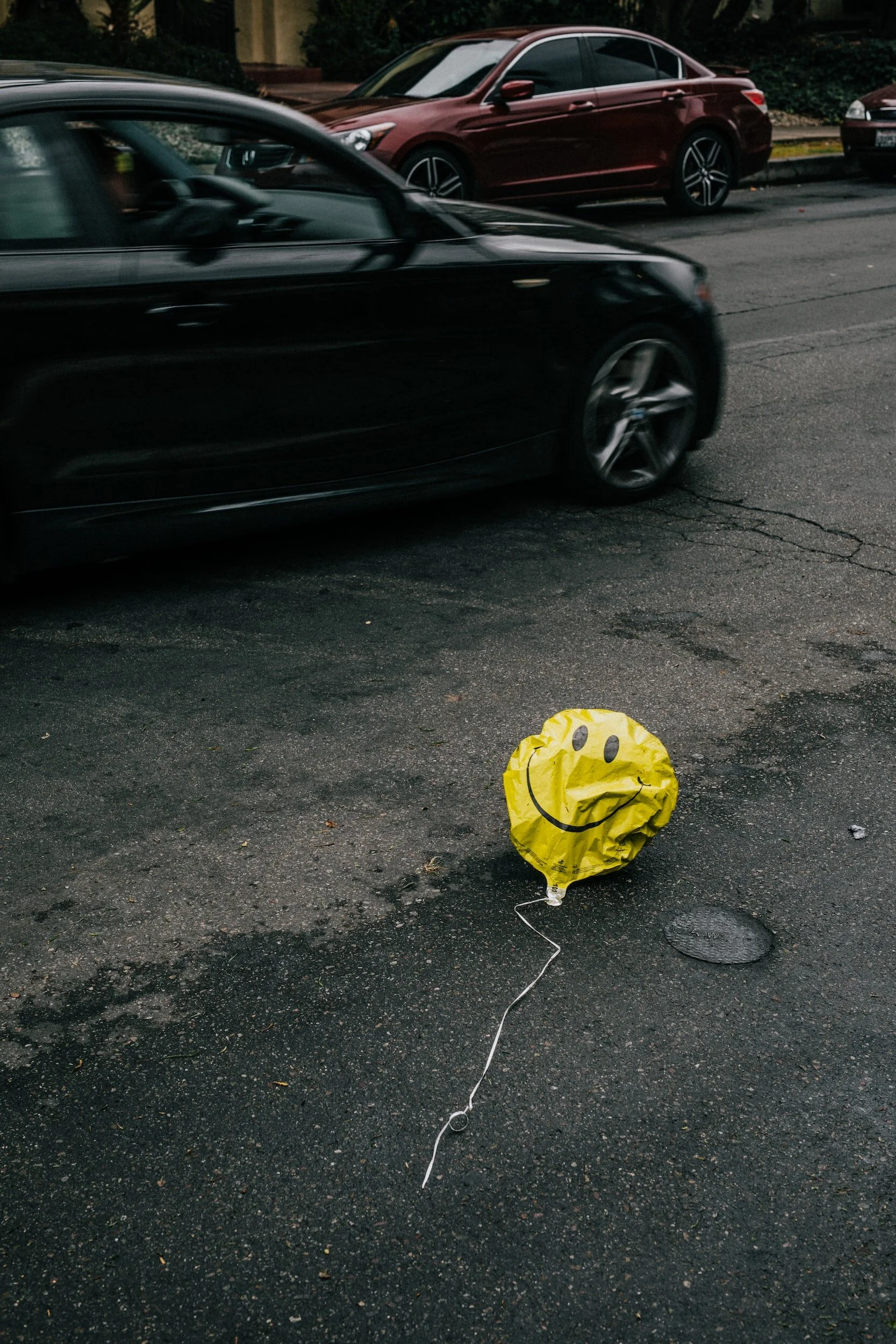 Ein gelber, lachender Ballon liegt auf der Straße, während vorbeifahrende Autos vorbeifahren.