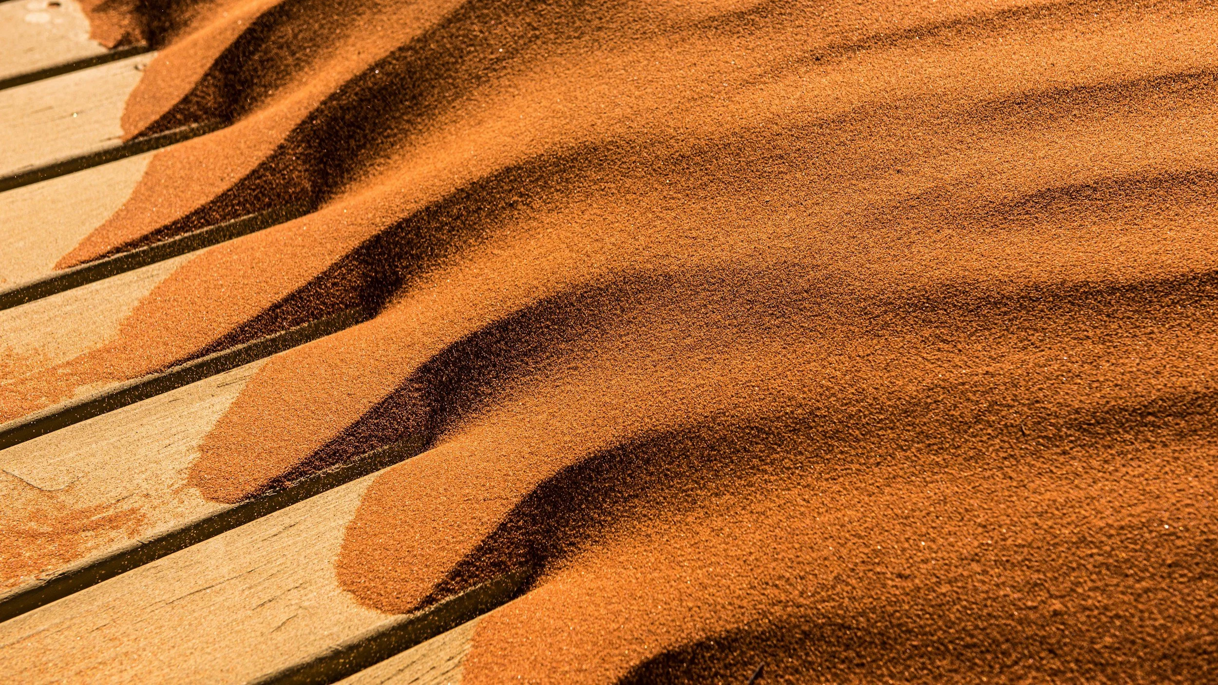 Rötlicher Sand mit Wellenmuster auf Holz – Symbol für innere Stille und Gelassenheit durch Hypnosetherapie bei generalisierter Angststörung Hamburg