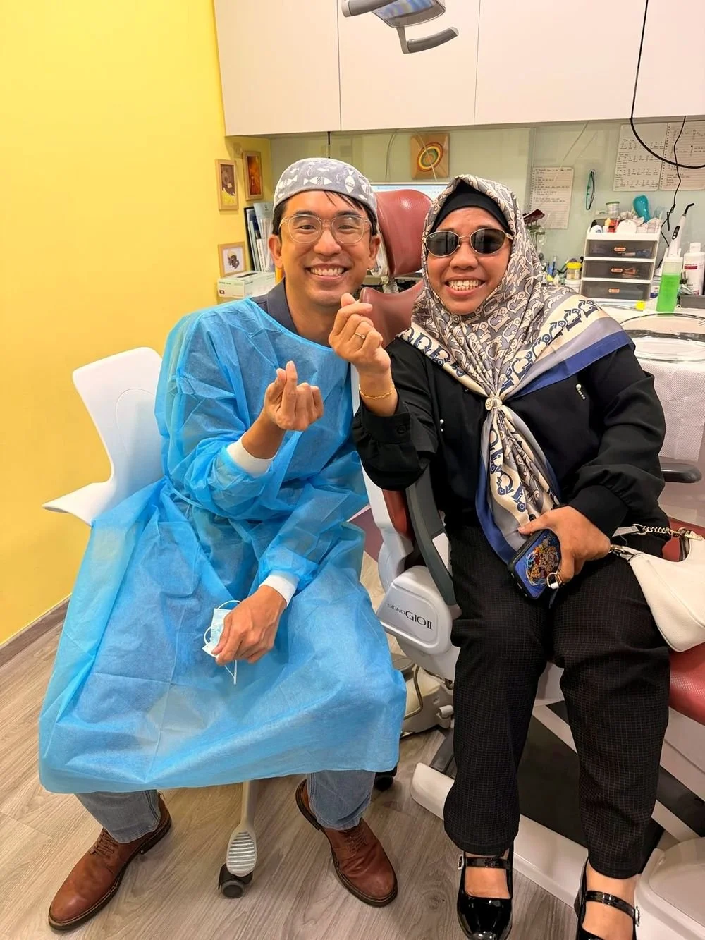 Dentist and a smiling patient in the clinic, both making a small hand gesture