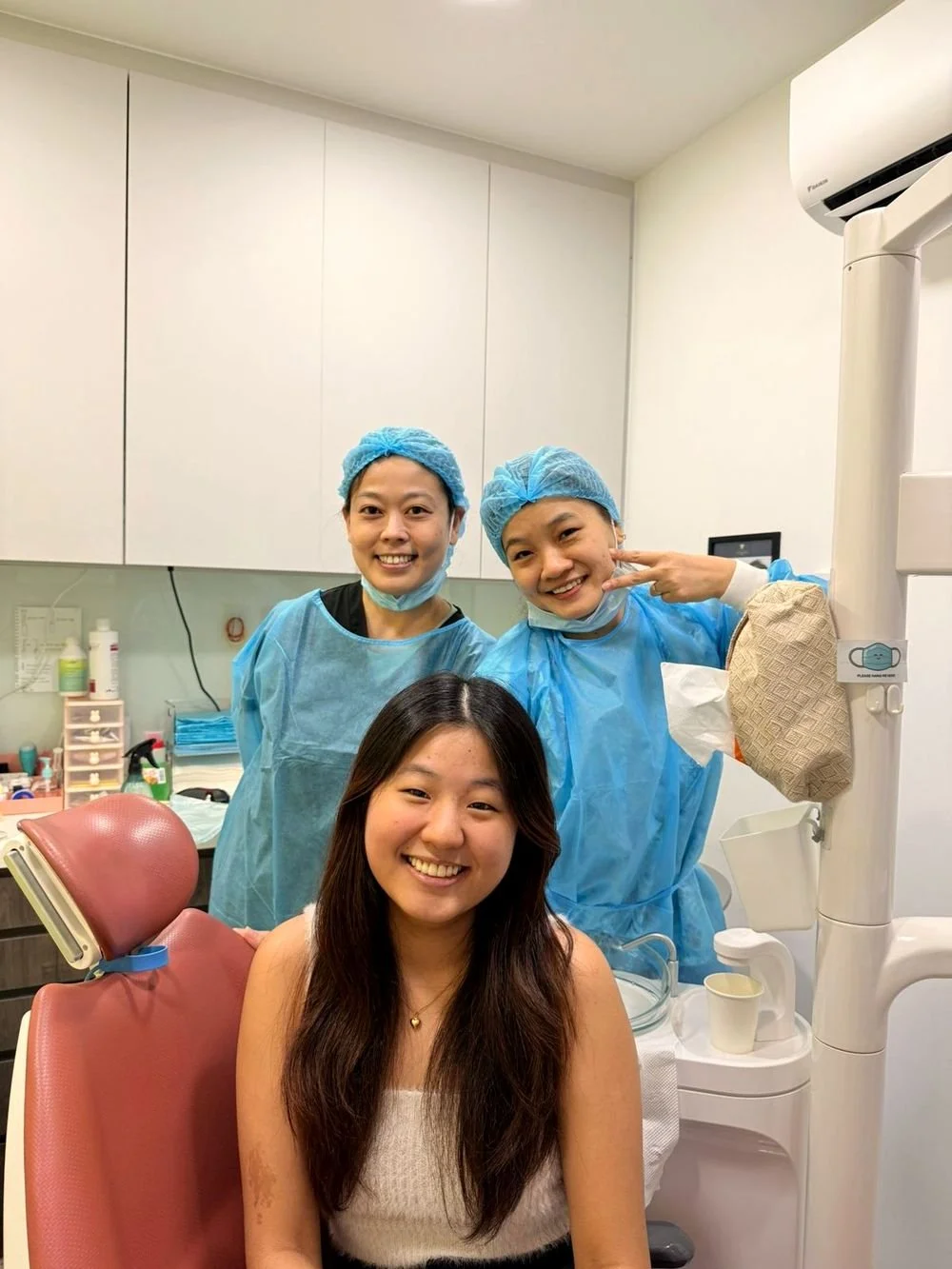 Two dental team members in blue gowns with a patient seated in the dental chair