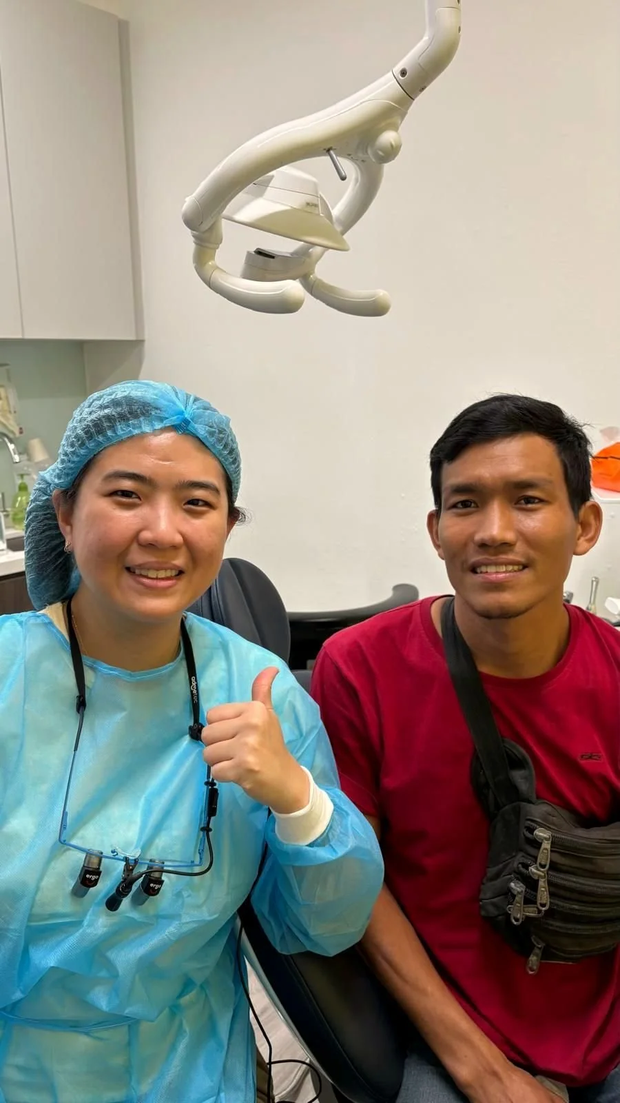 Dentist giving a thumbs up beside a smiling patient in a treatment room