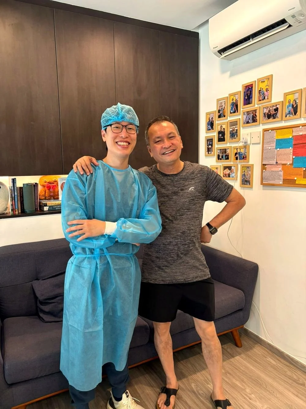 Dentist in a blue gown and cap standing with a smiling patient in the clinic waiting area