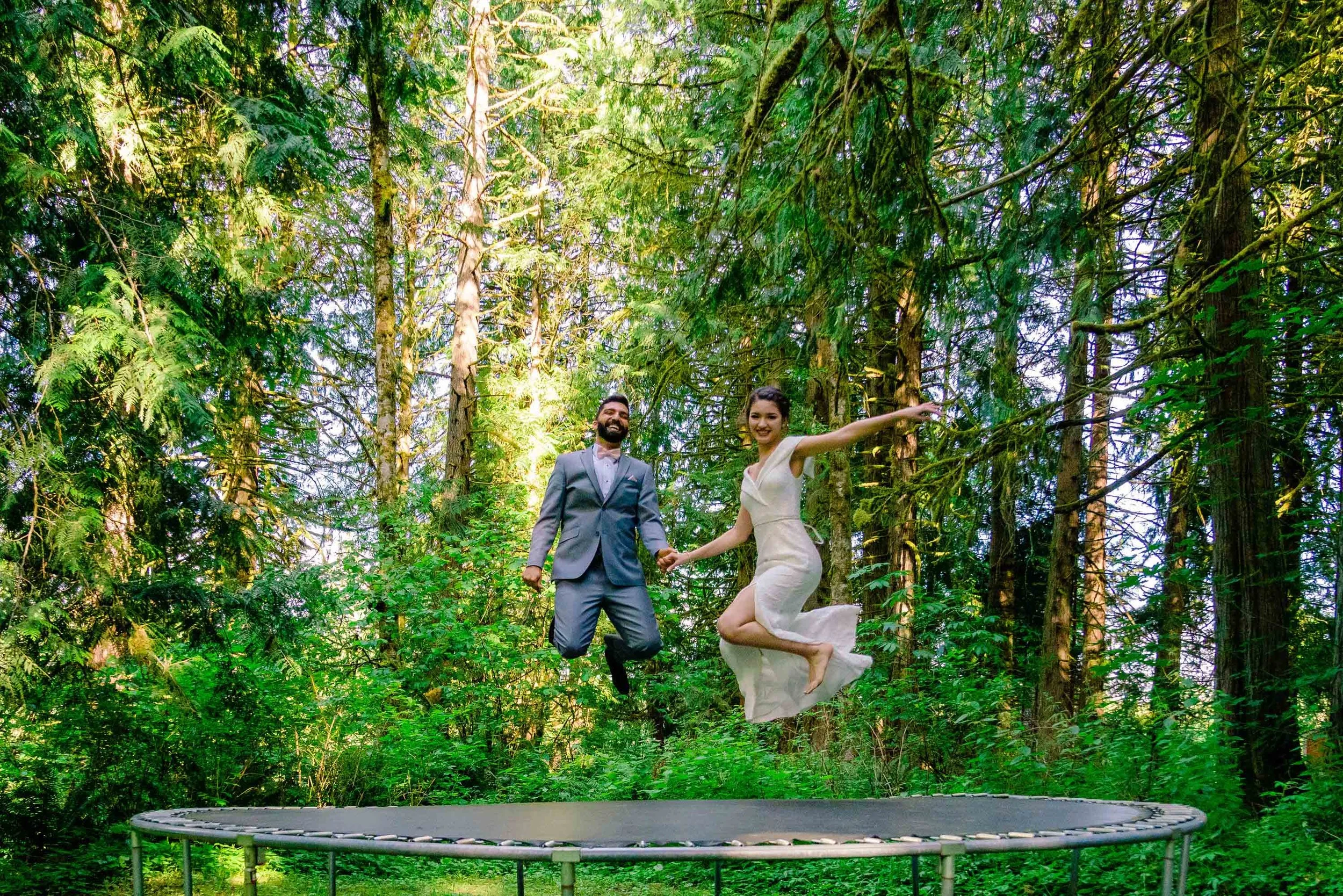 couple jumping in wedding clothing on trampoline in the forest