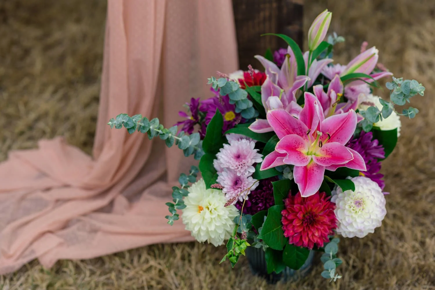 Colorful wedding florals with pink lilies, dahlias, and greenery arranged at wooden ceremony arch during elegant backyard wedding in Vancouver, Washington.
