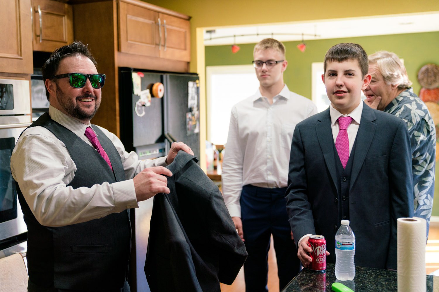 Groom getting ready with family in kitchen before backyard wedding in Vancouver WA, wearing gray suit and bright pink tie during relaxed at-home wedding morning.