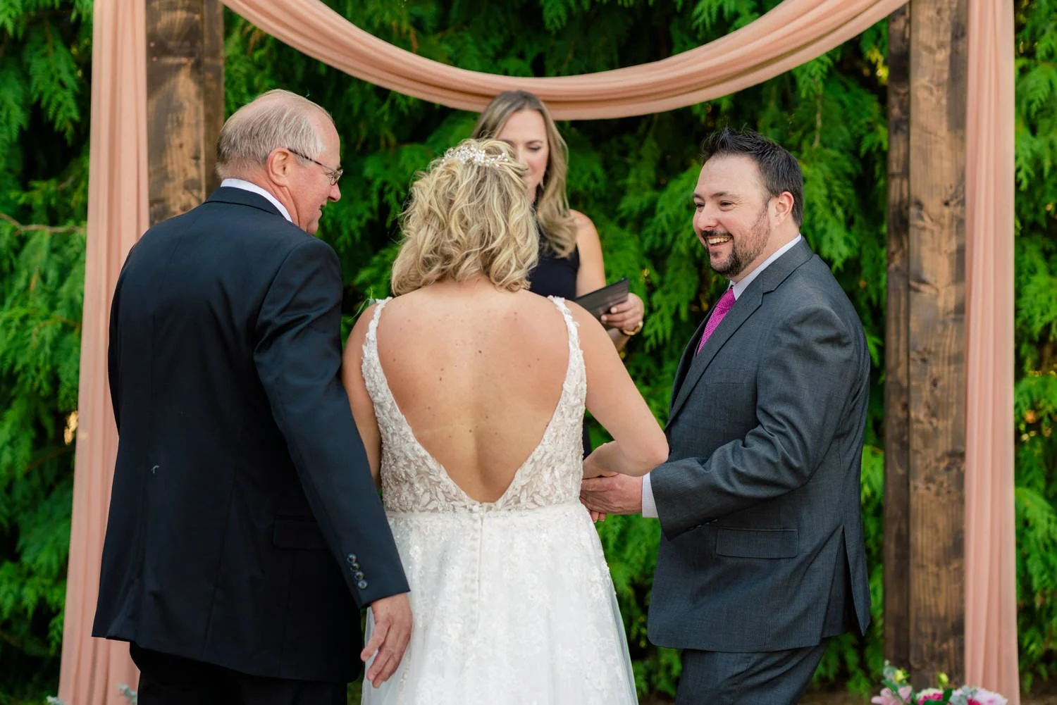 Bride’s father joining hands with groom during outdoor backyard wedding ceremony under wooden arch in Vancouver, Washington.