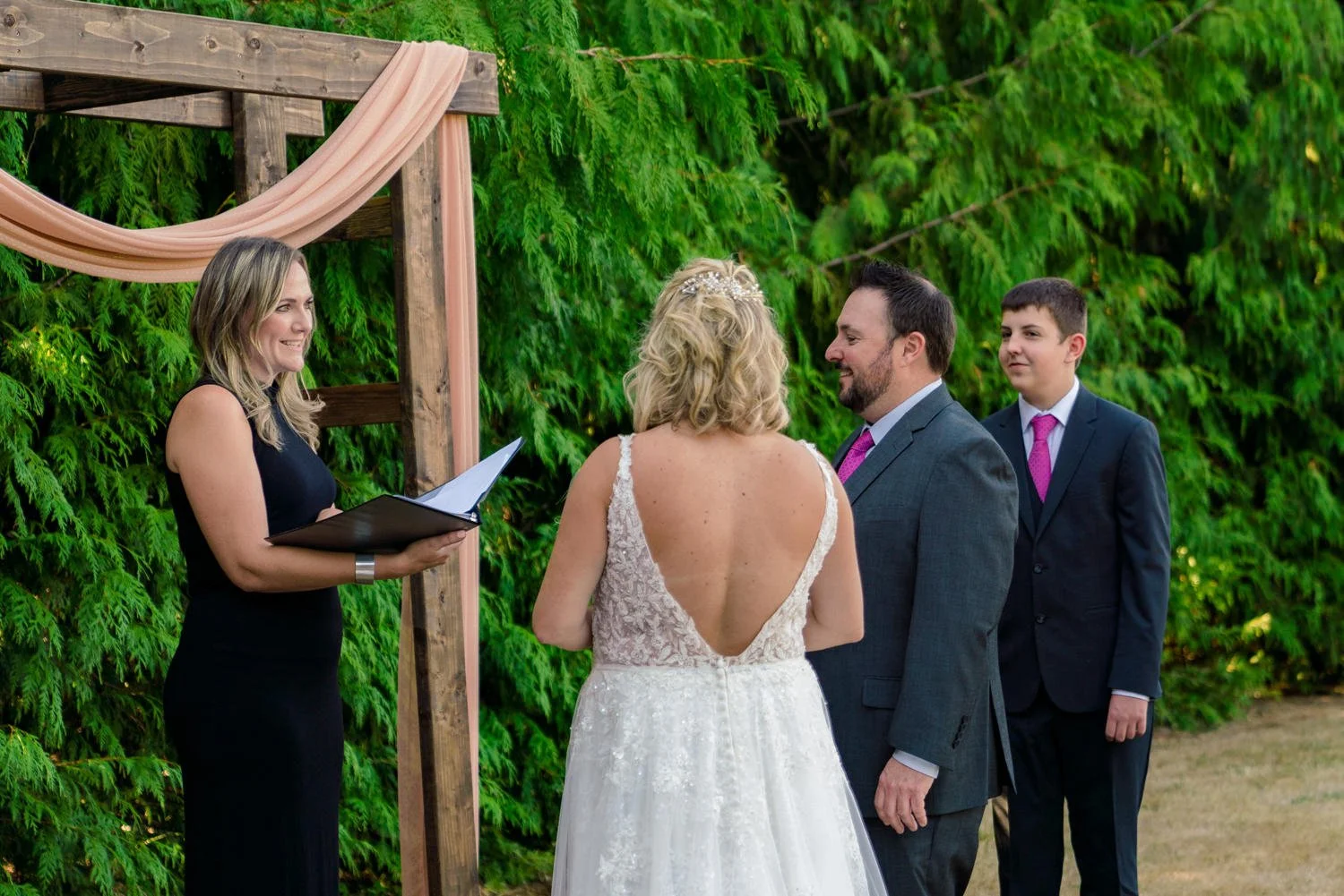 Bride and groom exchanging vows under wooden arch during simple backyard wedding ceremony in Vancouver WA.