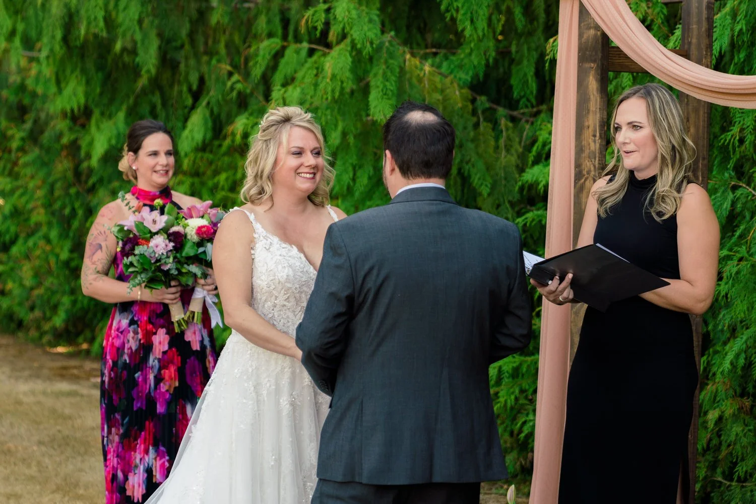 Bride and groom exchanging vows under wooden arch during simple backyard wedding ceremony in Vancouver WA.