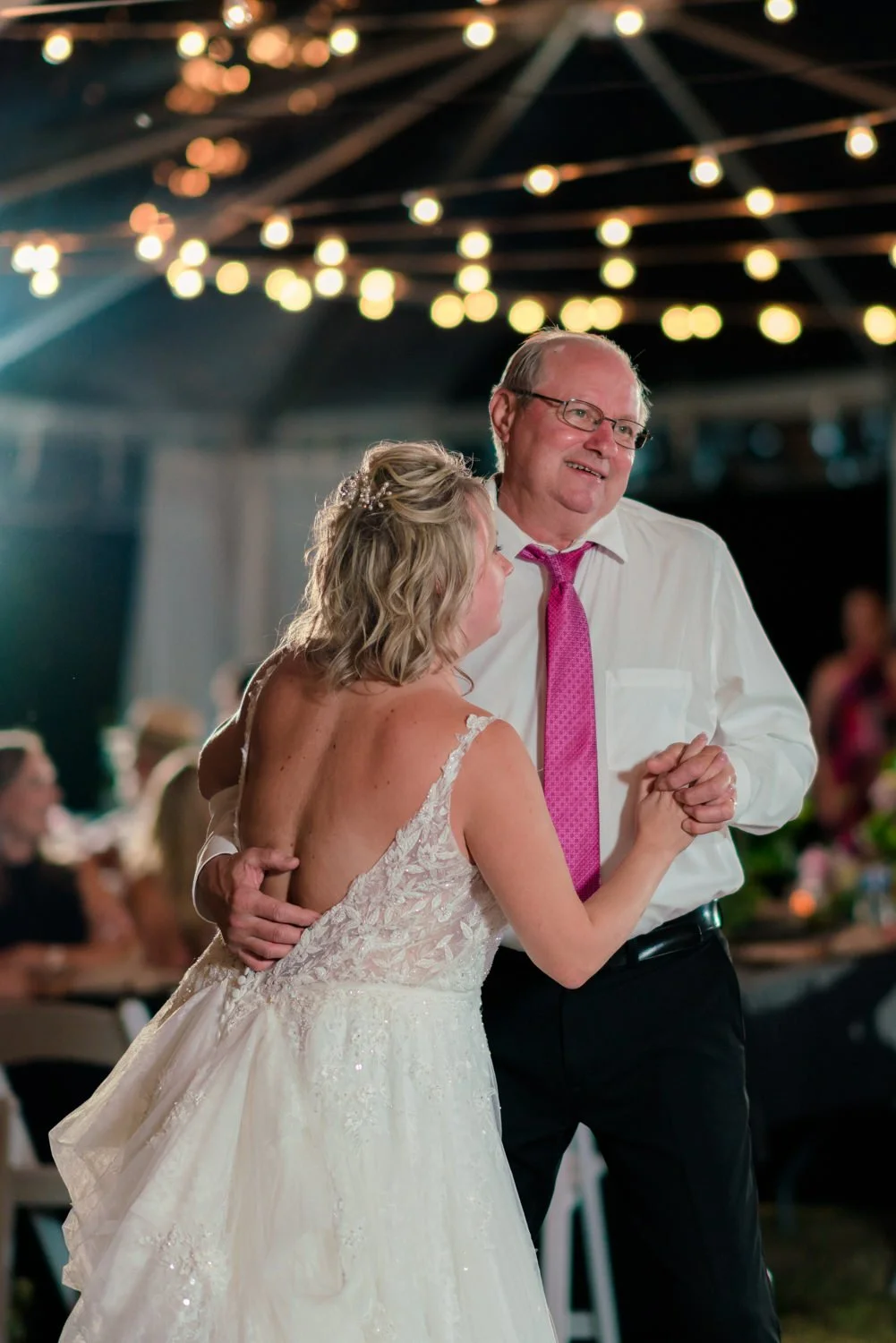 Bride sharing an emotional father daughter dance under string lights at a backyard wedding in Vancouver Washington, intimate reception moment beneath a clear tent at night.