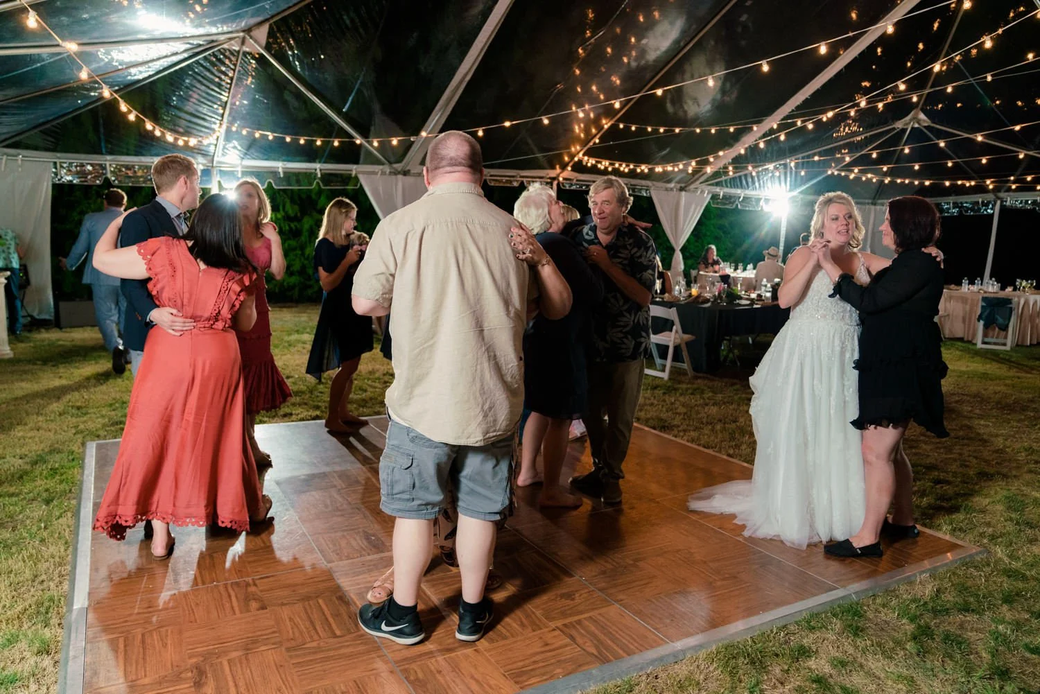 Bride greeting guests at their reception table under string lights at a backyard wedding in Vancouver Washington, candid nighttime celebration moment.