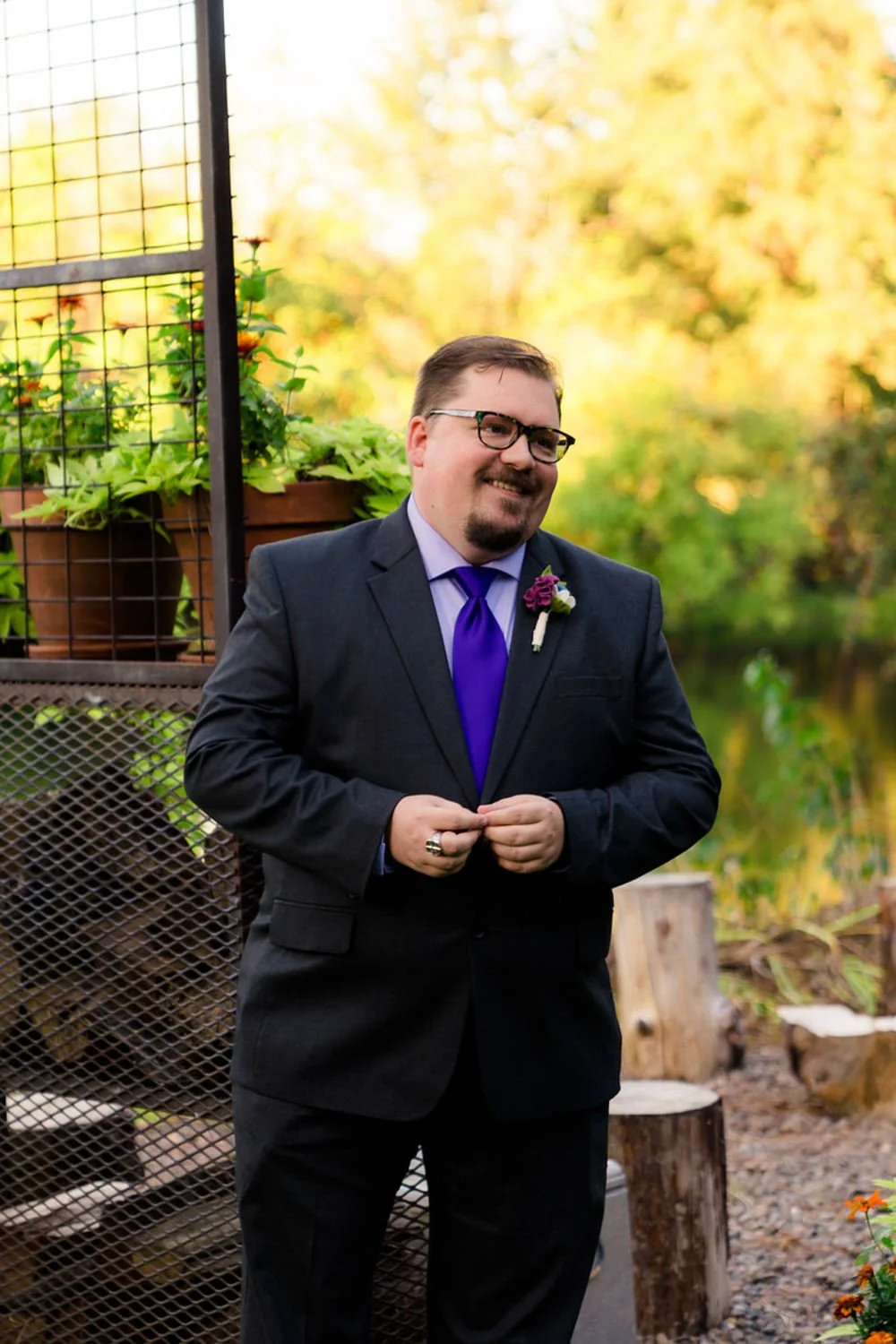 Groom smiling during a simple backyard elopement in Clackamas, Oregon, wearing a dark suit with a purple tie and boutonniere.