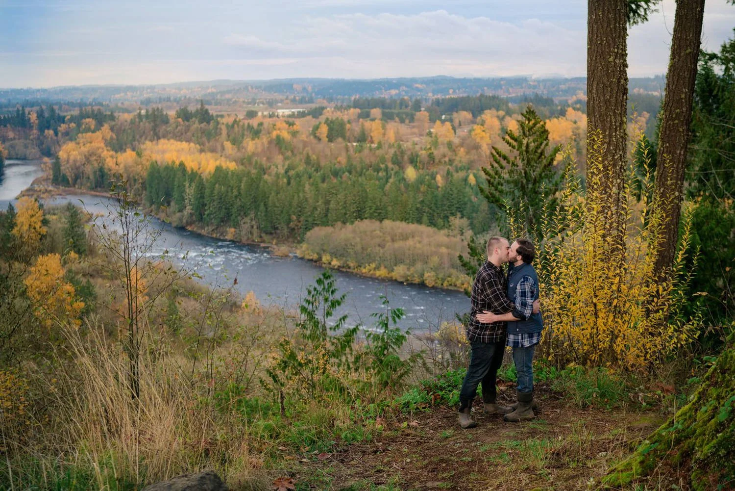 Couple sharing a kiss on a wooden overlook with a calm lake and forest reflections during a fall engagement session.