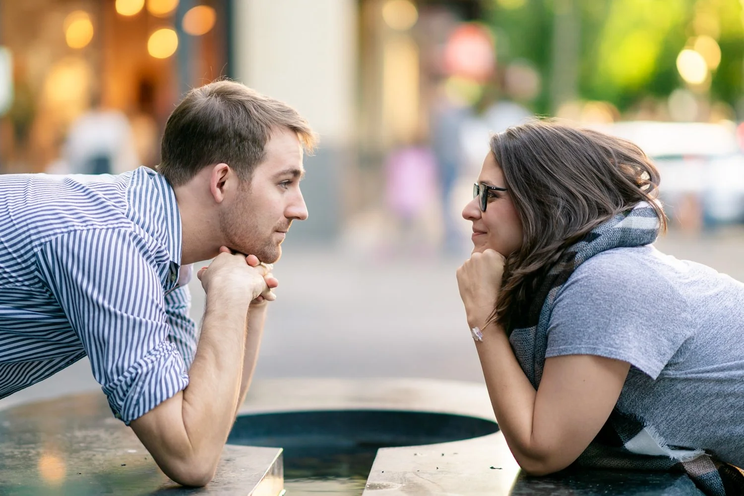 Couple leaning across a fountain, resting their chins on their hands and smiling at each other during a playful and romantic Portland engagement session.