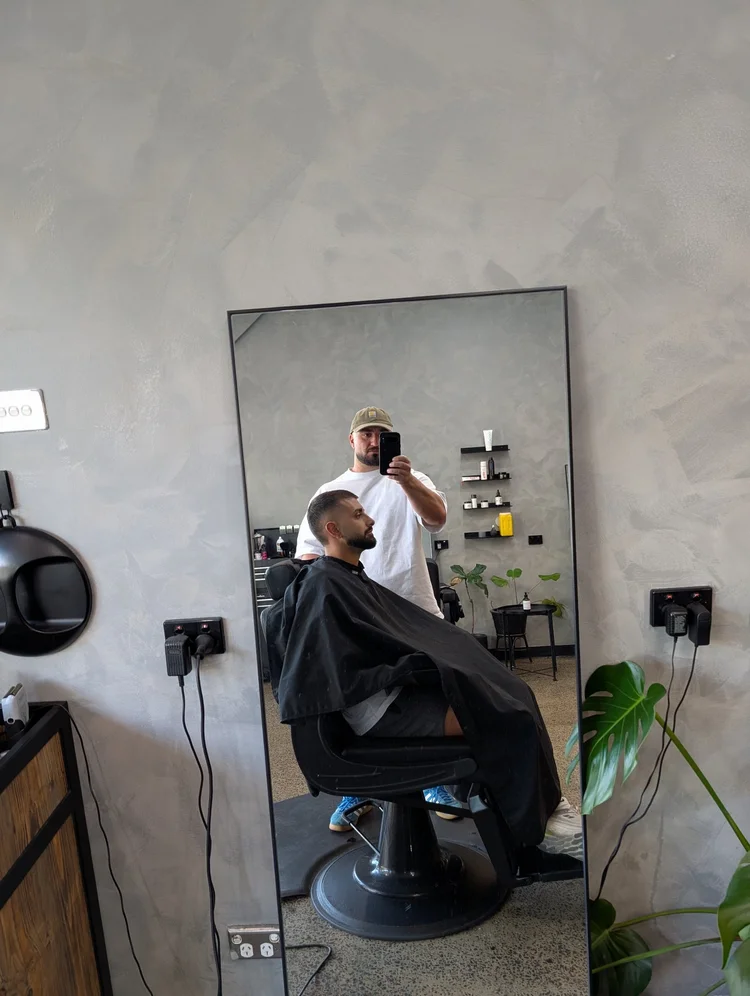 Barber cutting hair by the front window of Bsharp Barbershop, Lygon Street visible outside