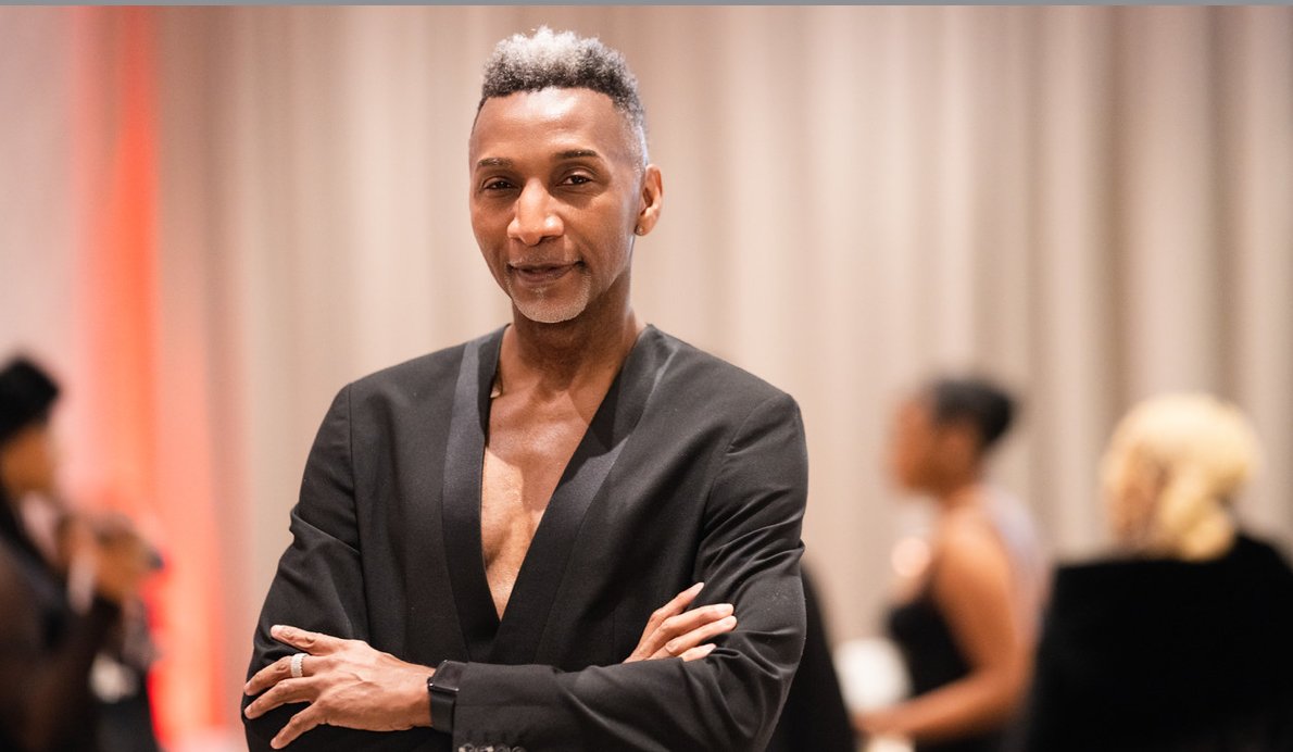 Three women dressed in elegant evening attire posing together at an event. The woman in the middle is holding a clear glass award and a gift bag.