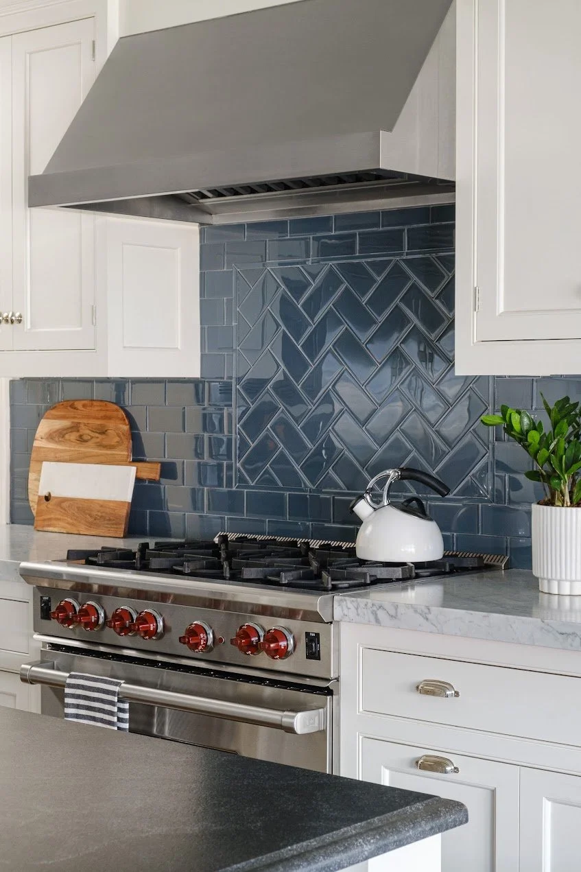 Classic white cabinets, Carrera countertops, and traditional bin pulls combine with glass tile and modern light fixtures in the transitional kitchen design