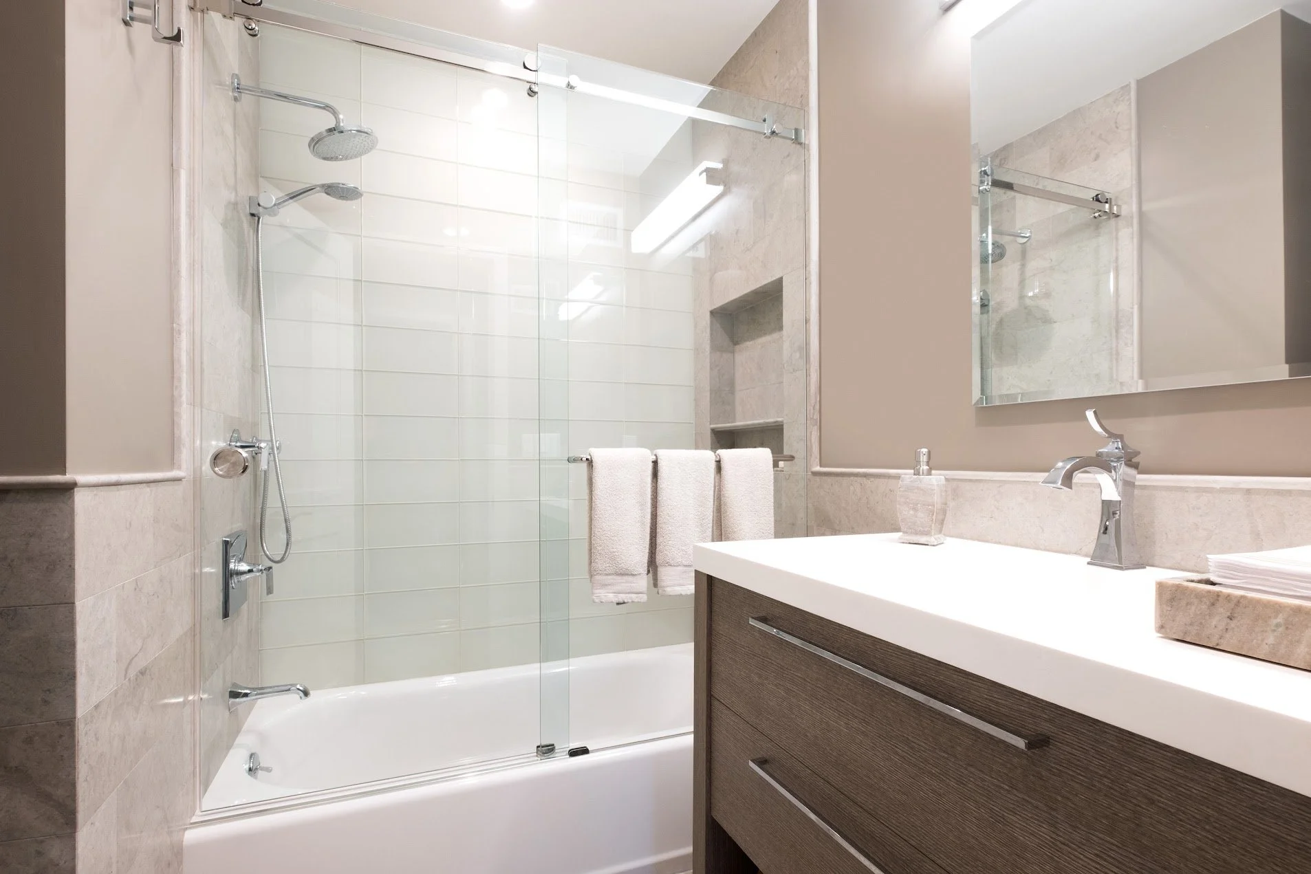 Putnam Valley lake house bathroom renovation featuring limestone tile, frameless glass shower, custom vanity, quartz countertop, and modern chrome plumbing fixtures.
