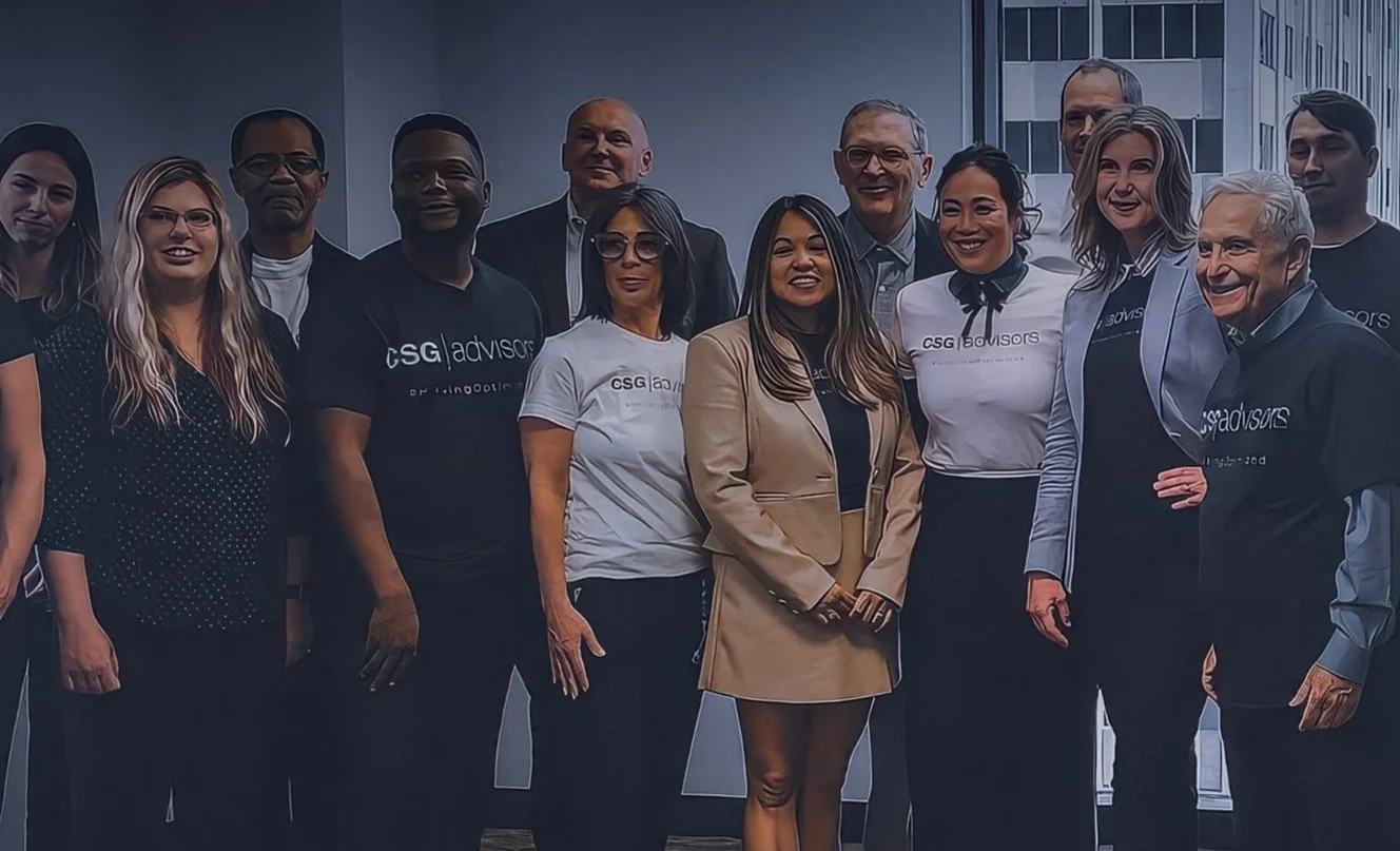 Group of diverse professionals standing together in an office with large windows and cityscape view.