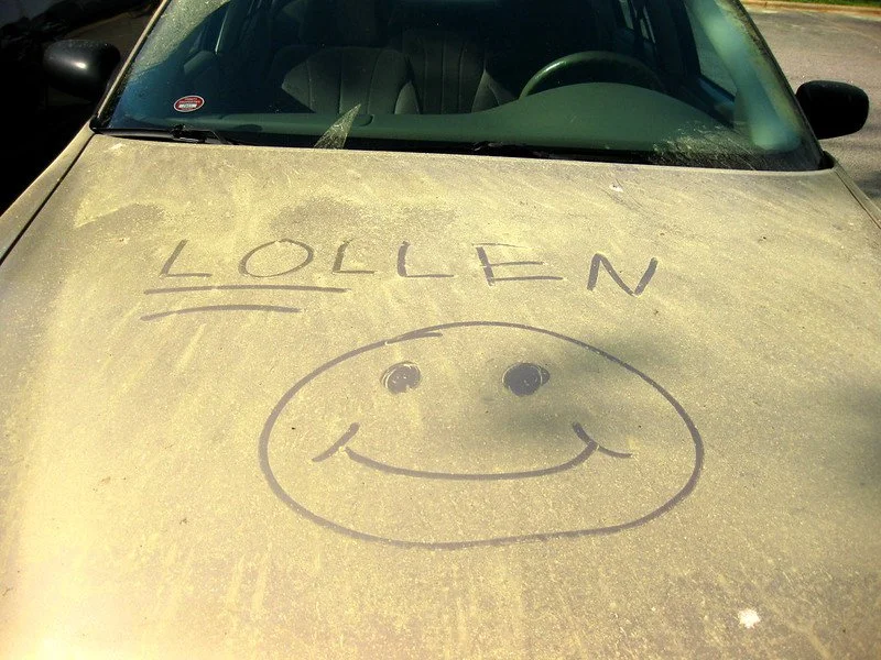 Car covered in pollen with a smiley face and the word "LOLLEN" Written on it.