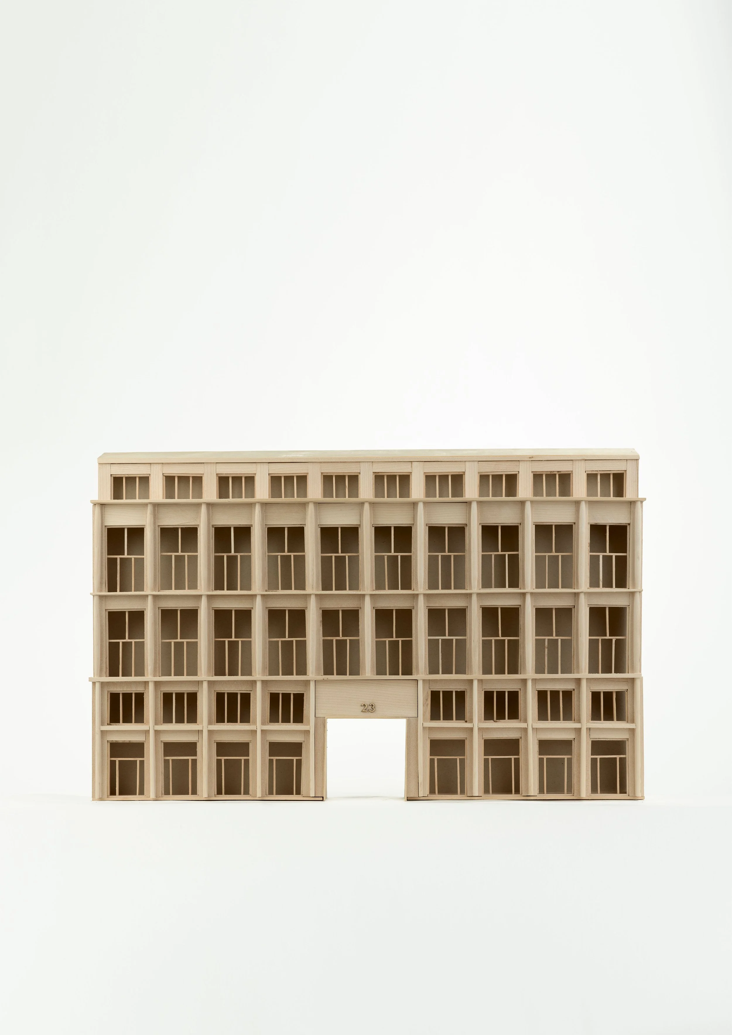A multi-story building model made of light-colored wood with multiple windows, set against a plain white background.