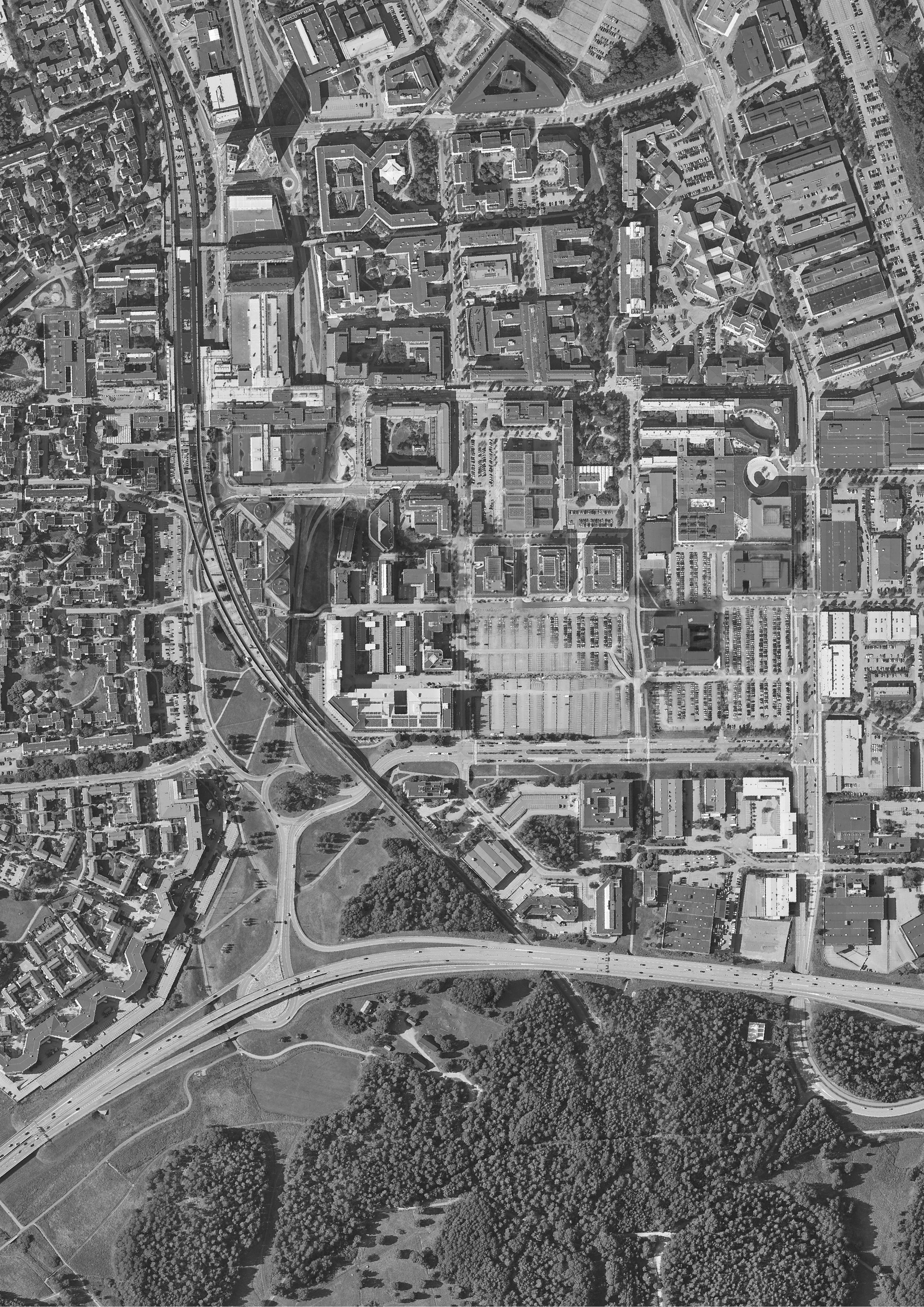 An aerial view of a city with numerous buildings, roads, highways, and green spaces, with a large park and dense clusters of trees at the bottom.