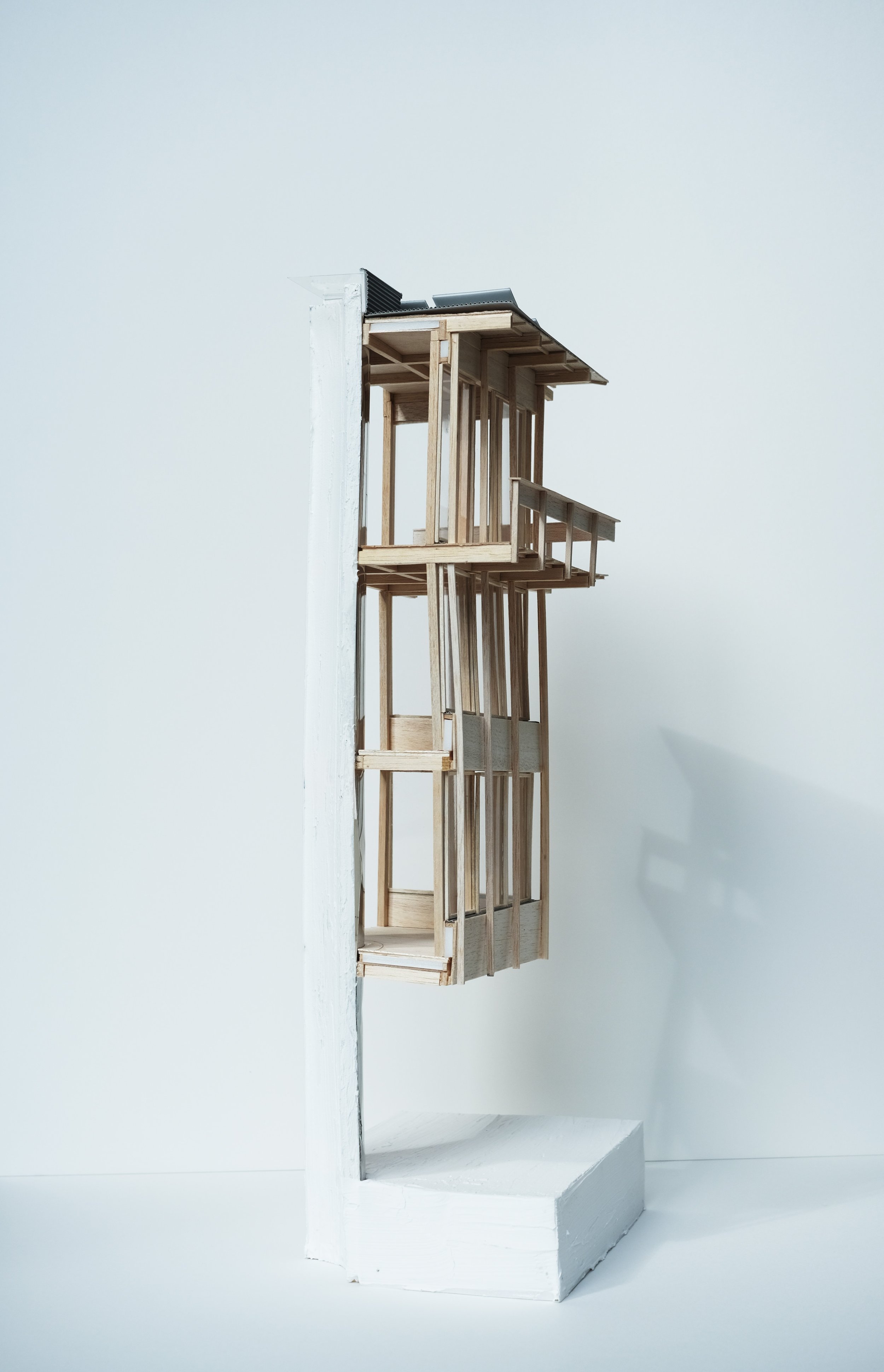 A scale model of a modern house on a white display platform against a white background, showcasing wood framing and partial roofing.