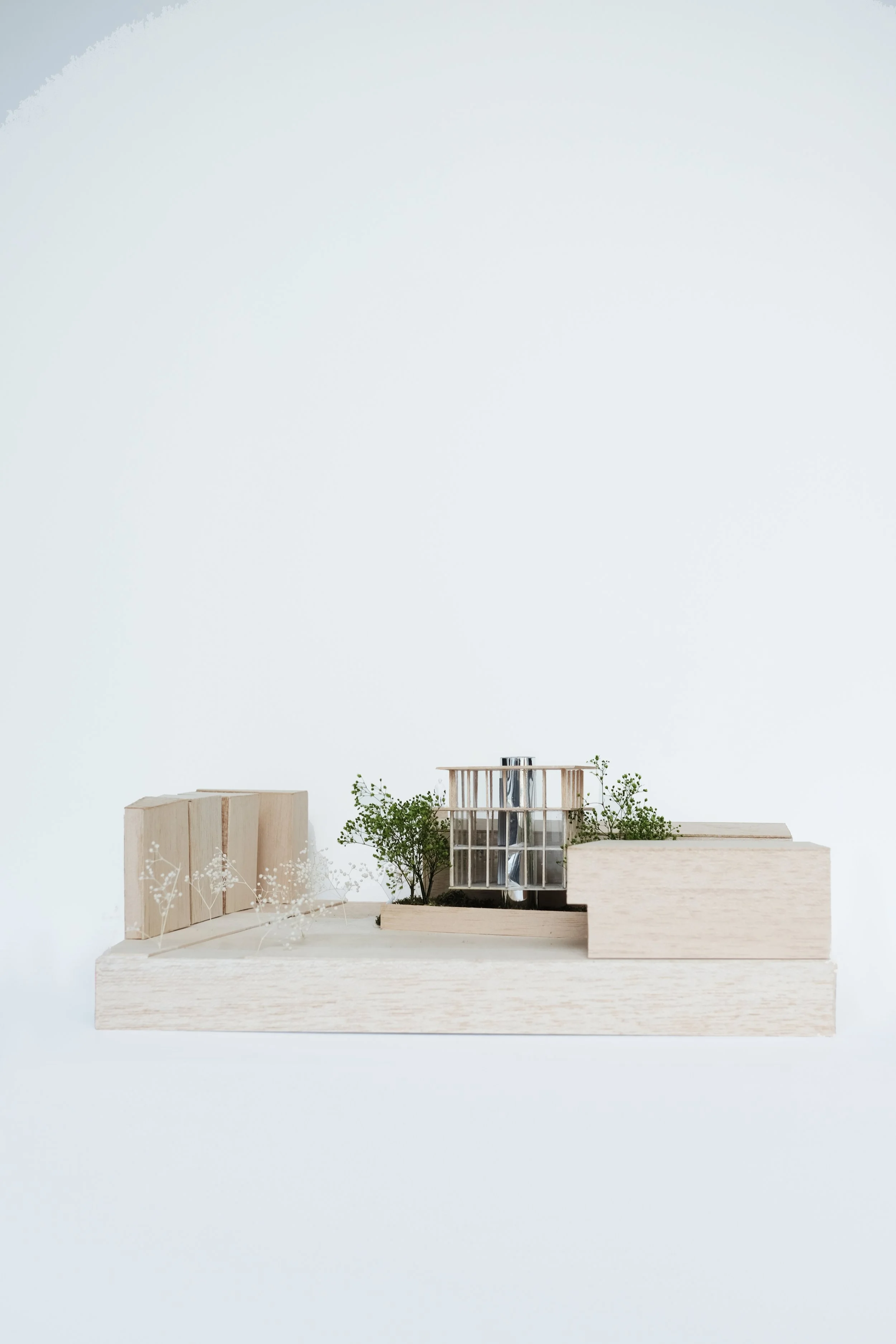 Architectural model featuring wooden and transparent structures with small trees on a white platform.
