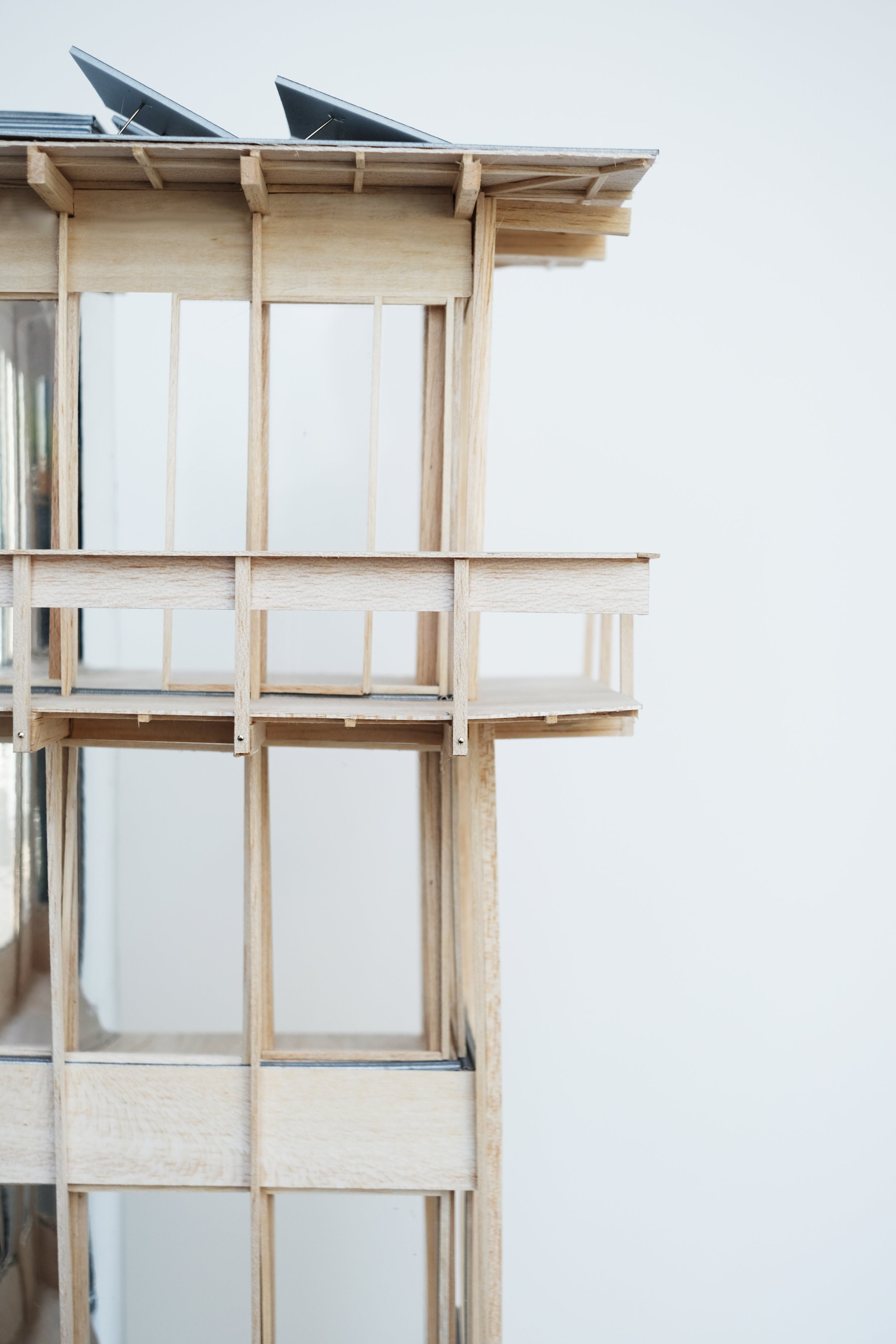 Close-up of a miniature wooden house model with a balcony and slanted roof, placed against a plain white background.