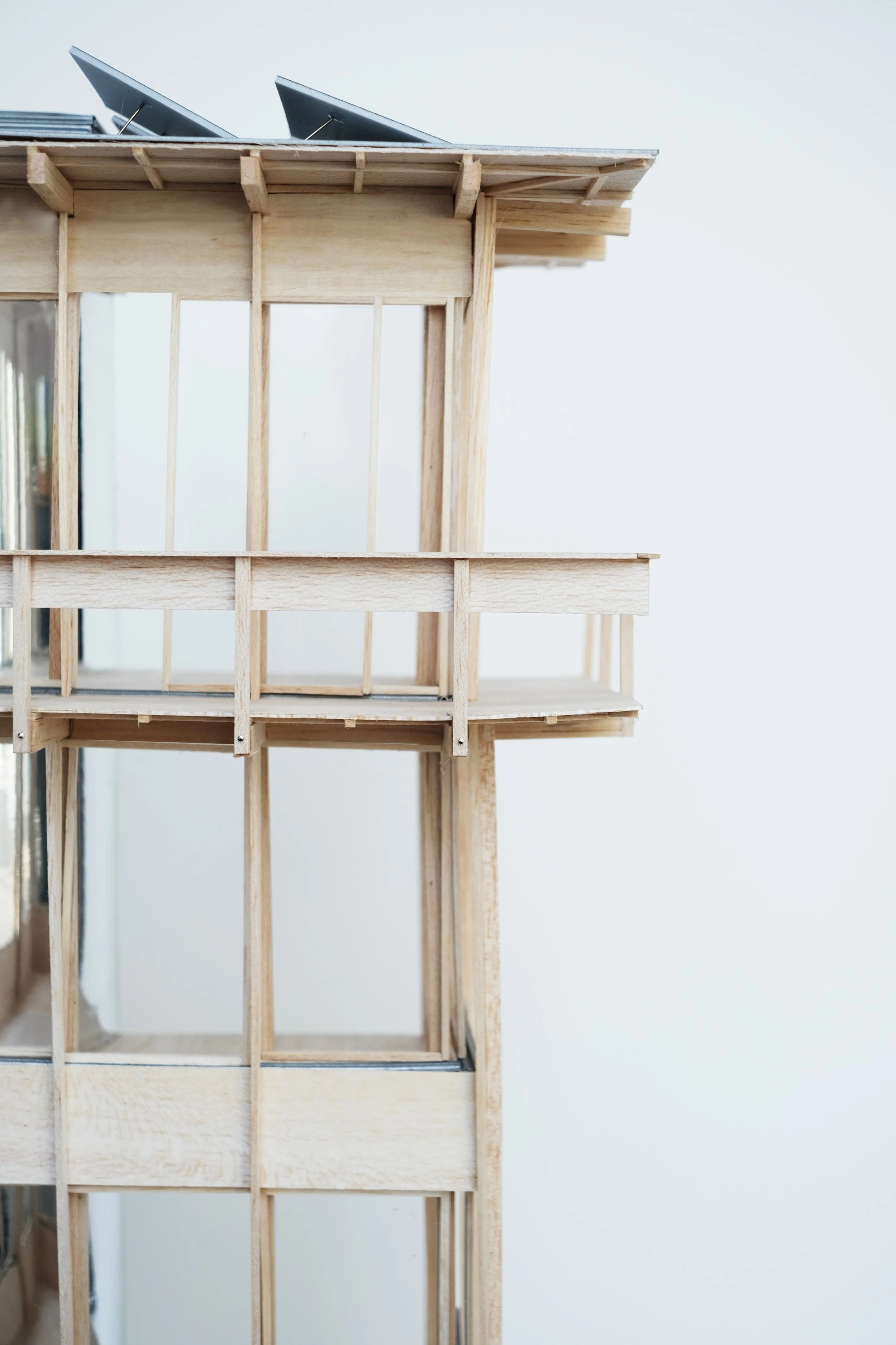 A detailed wooden architectural model of a house or building with a balcony and solar panels on the roof.