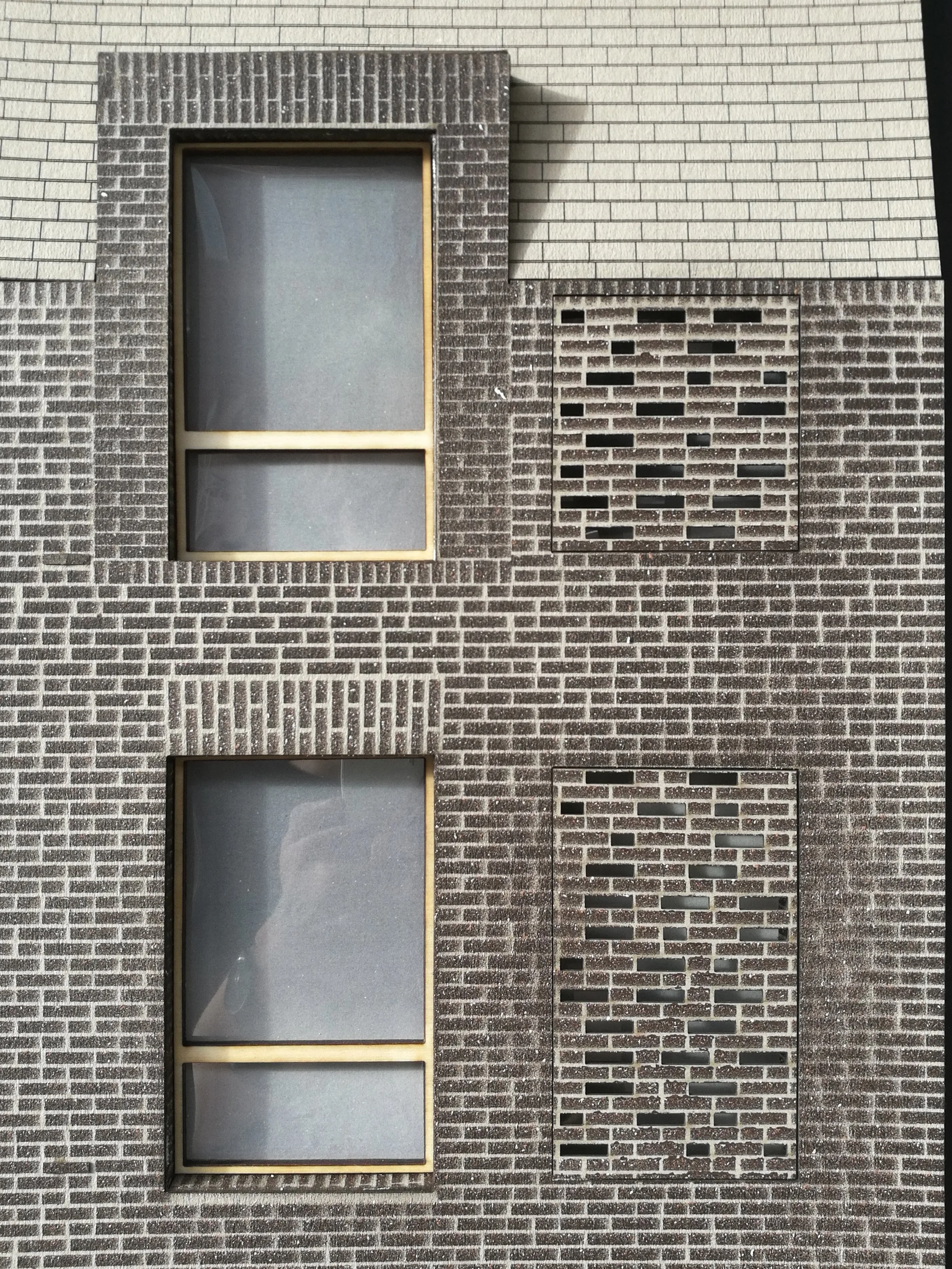 Close-up of a brick building with three rectangular windows, two of which are frosted glass and one with an interlocking brick pattern.