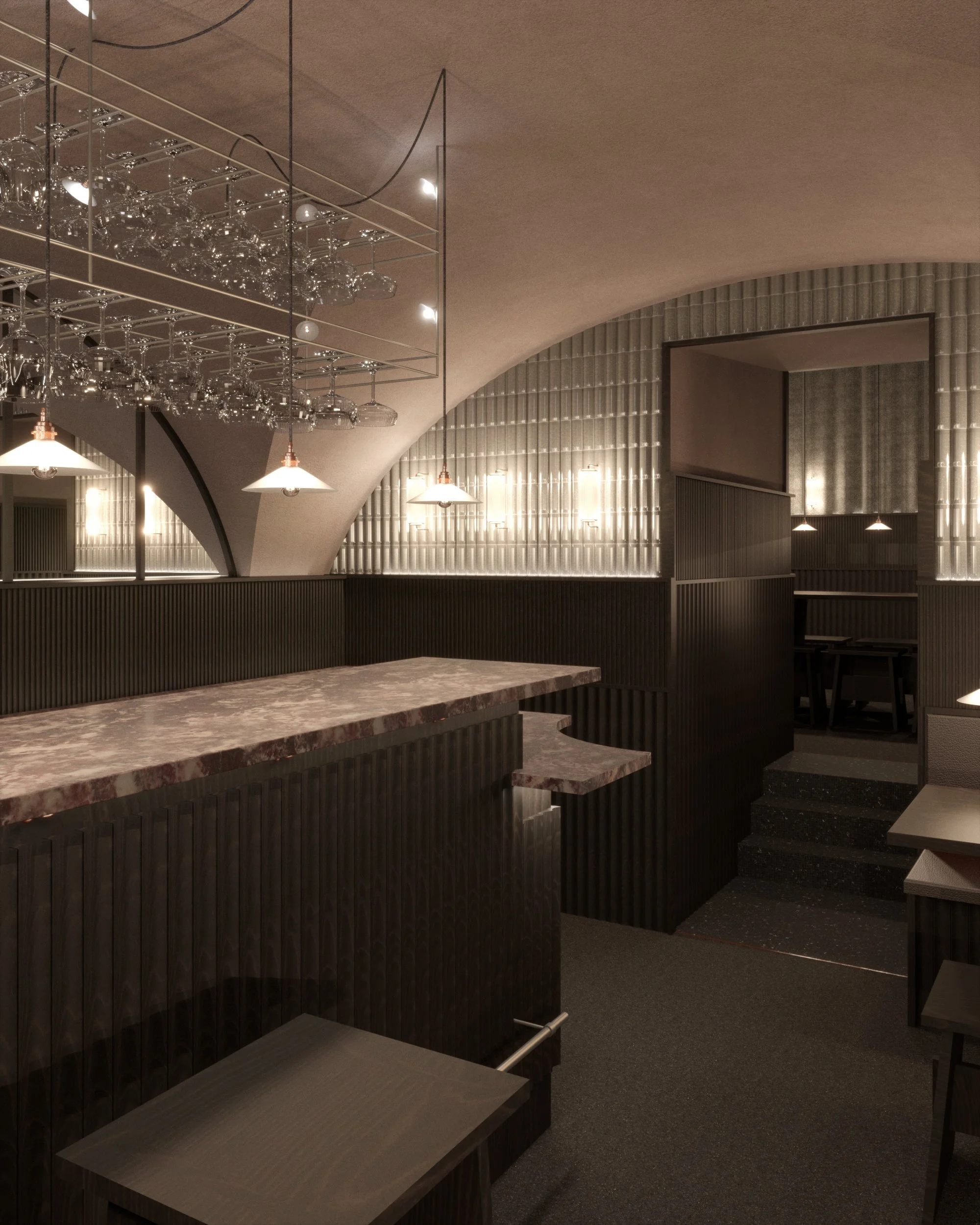 A modern interior space with a curved ceiling, illuminated by hanging pendant lights. There is a marble-topped bar with a dark, ribbed wooden front, and a shelf overhead with glassware hanging upside down. The walls are lined with vertically ridged m