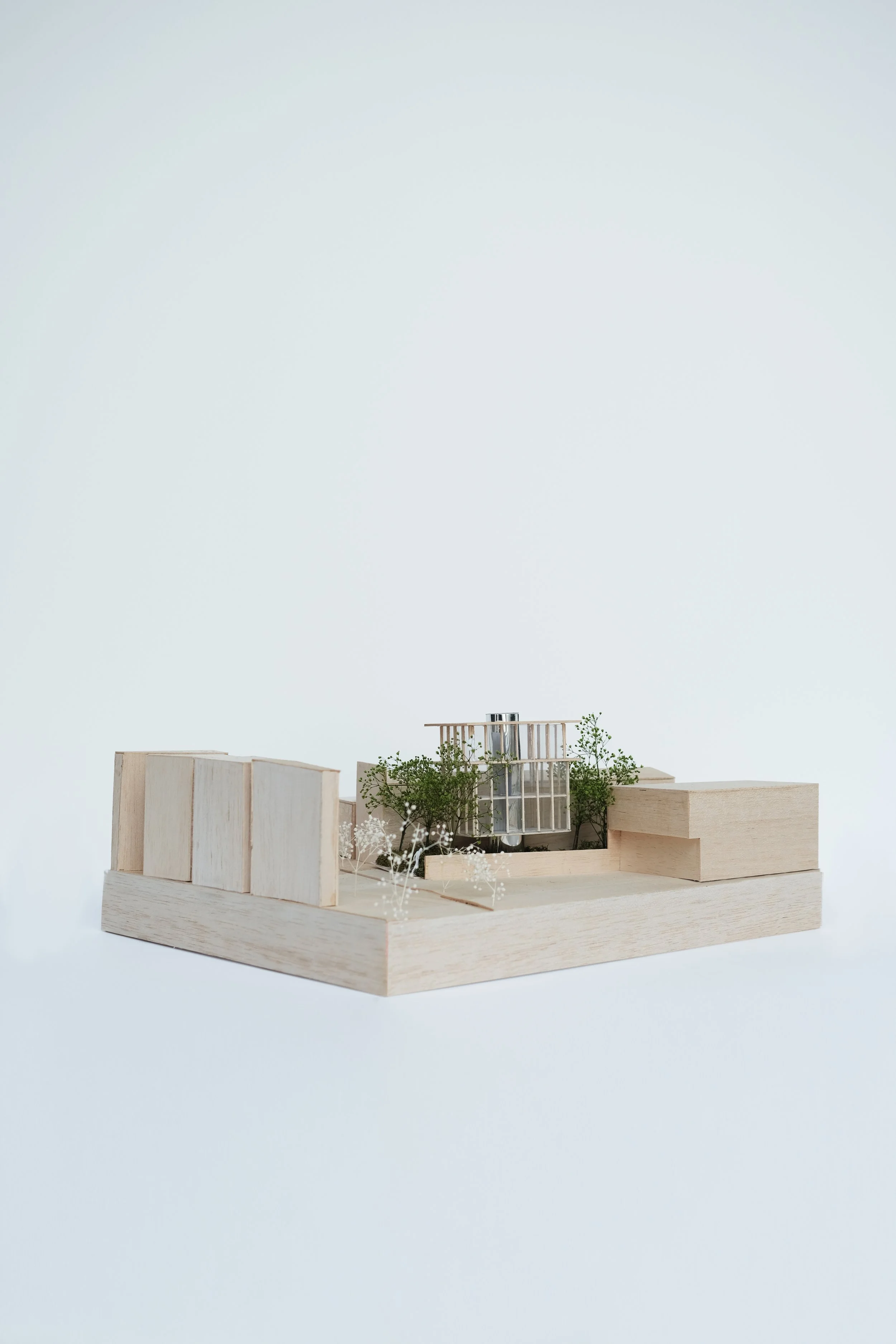 An architectural model made of wood, featuring multiple small buildings and green trees.
