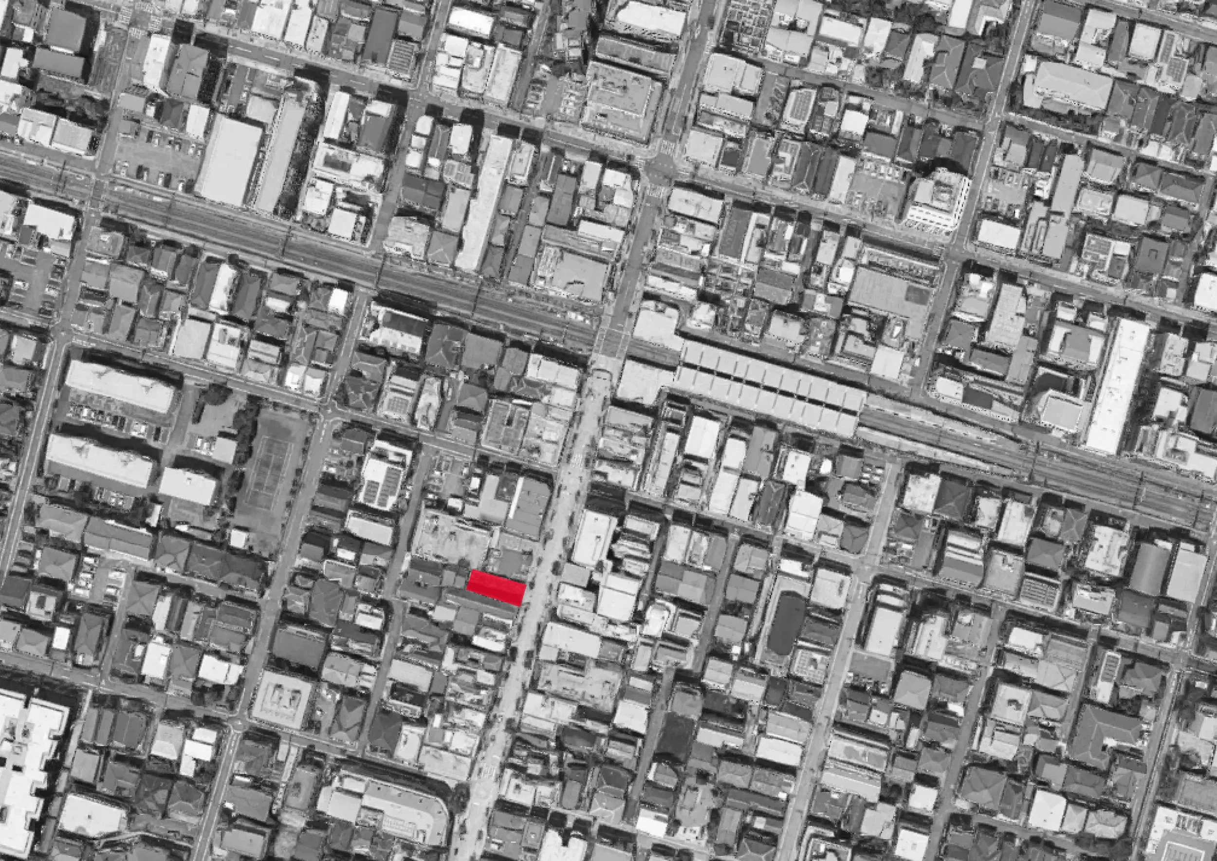 An aerial grayscale map of a city grid showing numerous buildings, streets, and a railway track. A red rectangle highlights a specific location on the map.