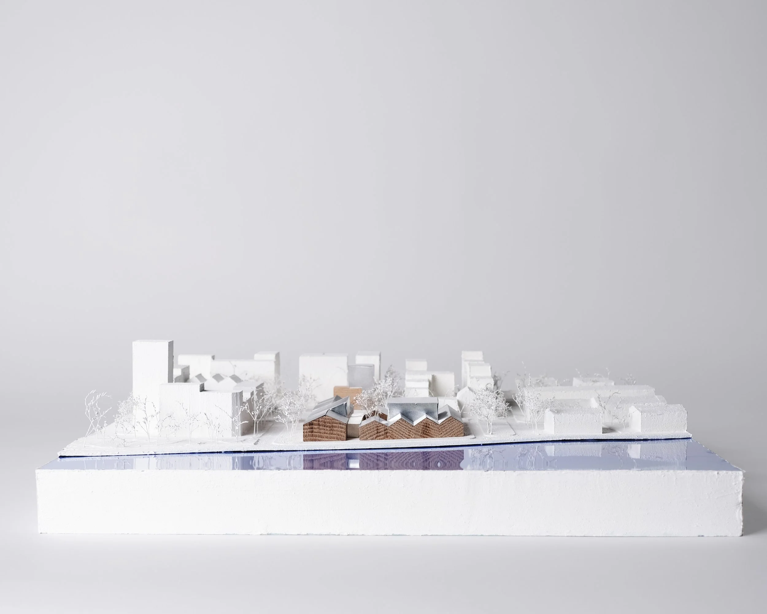 Architectural model of a building complex with trees, set on a white base against a plain light gray background.