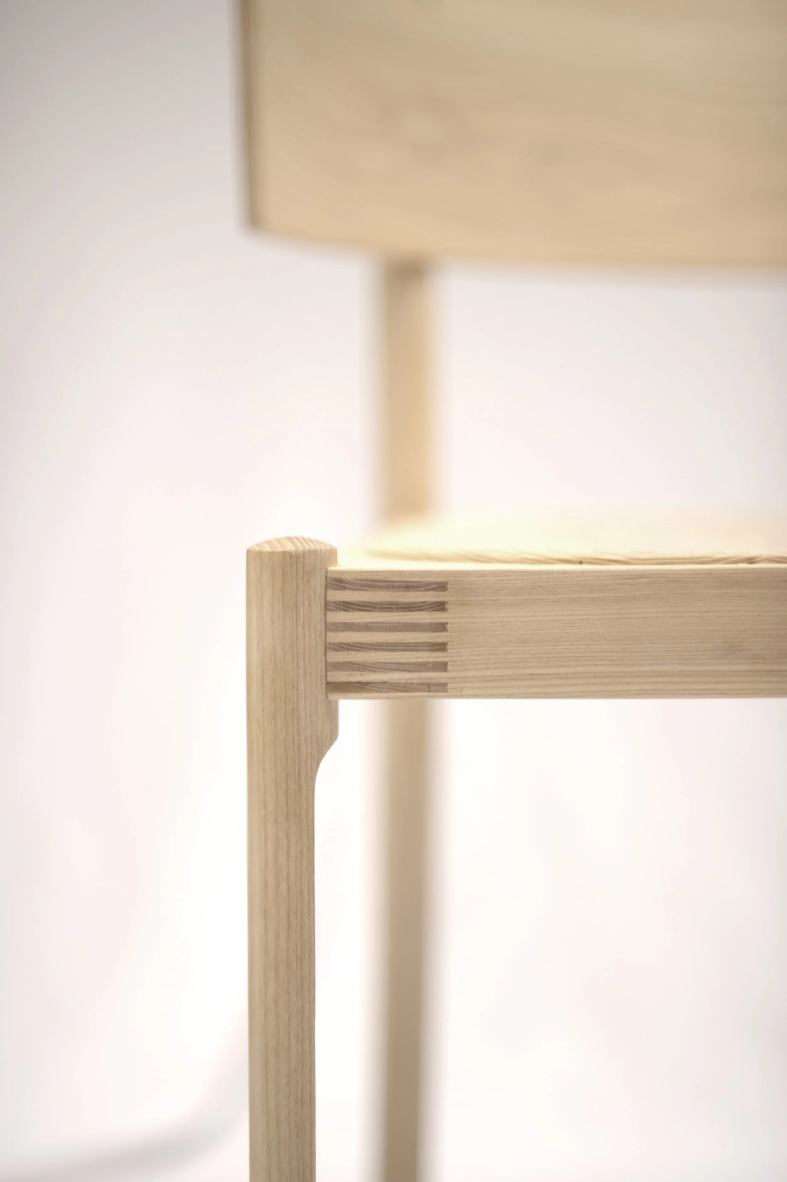 Close-up of light wooden furniture, highlighting the corner and turn of a piece against a plain white background.