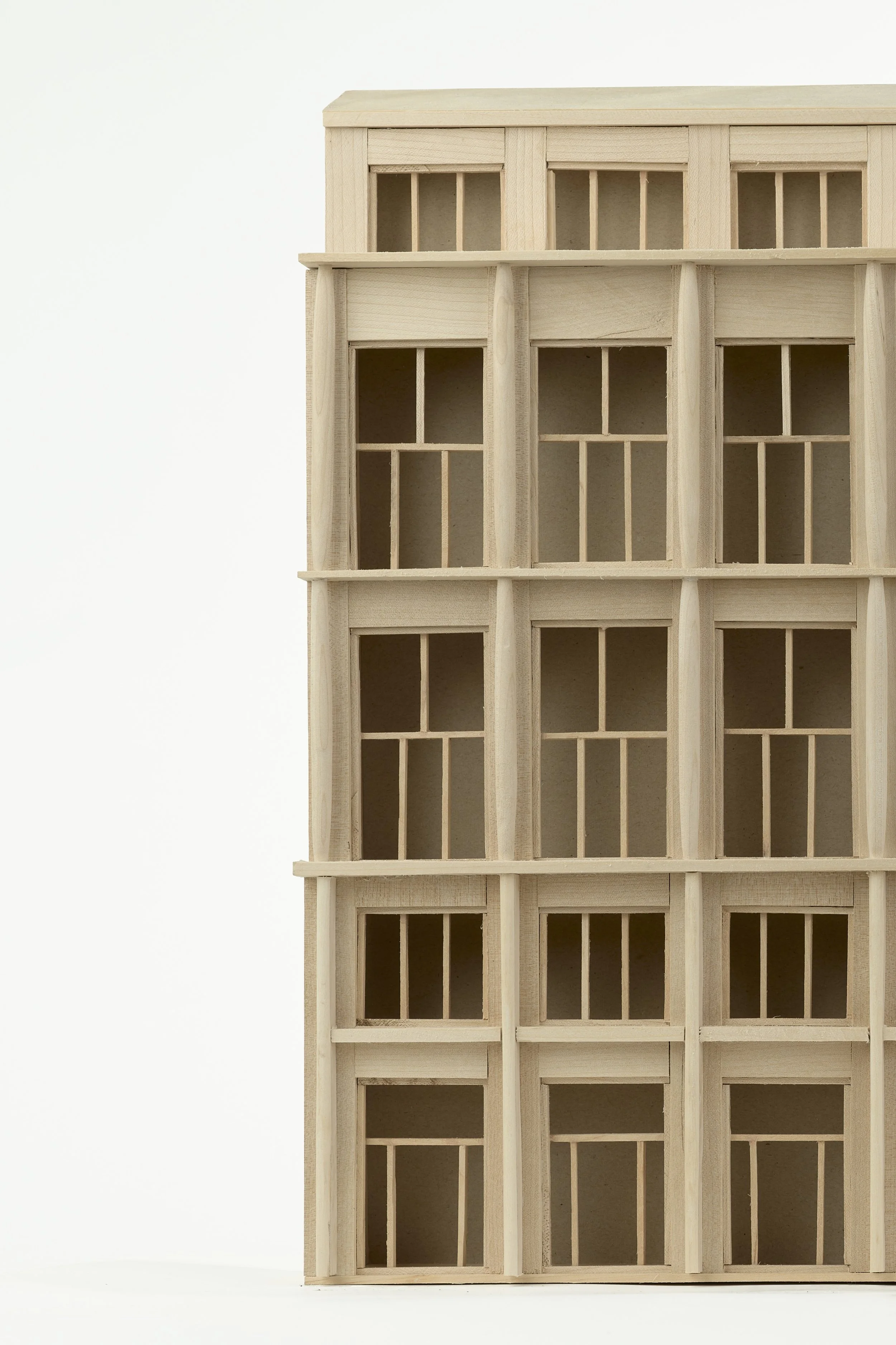 Multiple unpainted wooden dollhouses with small windows, arranged in a stack against a plain white background.