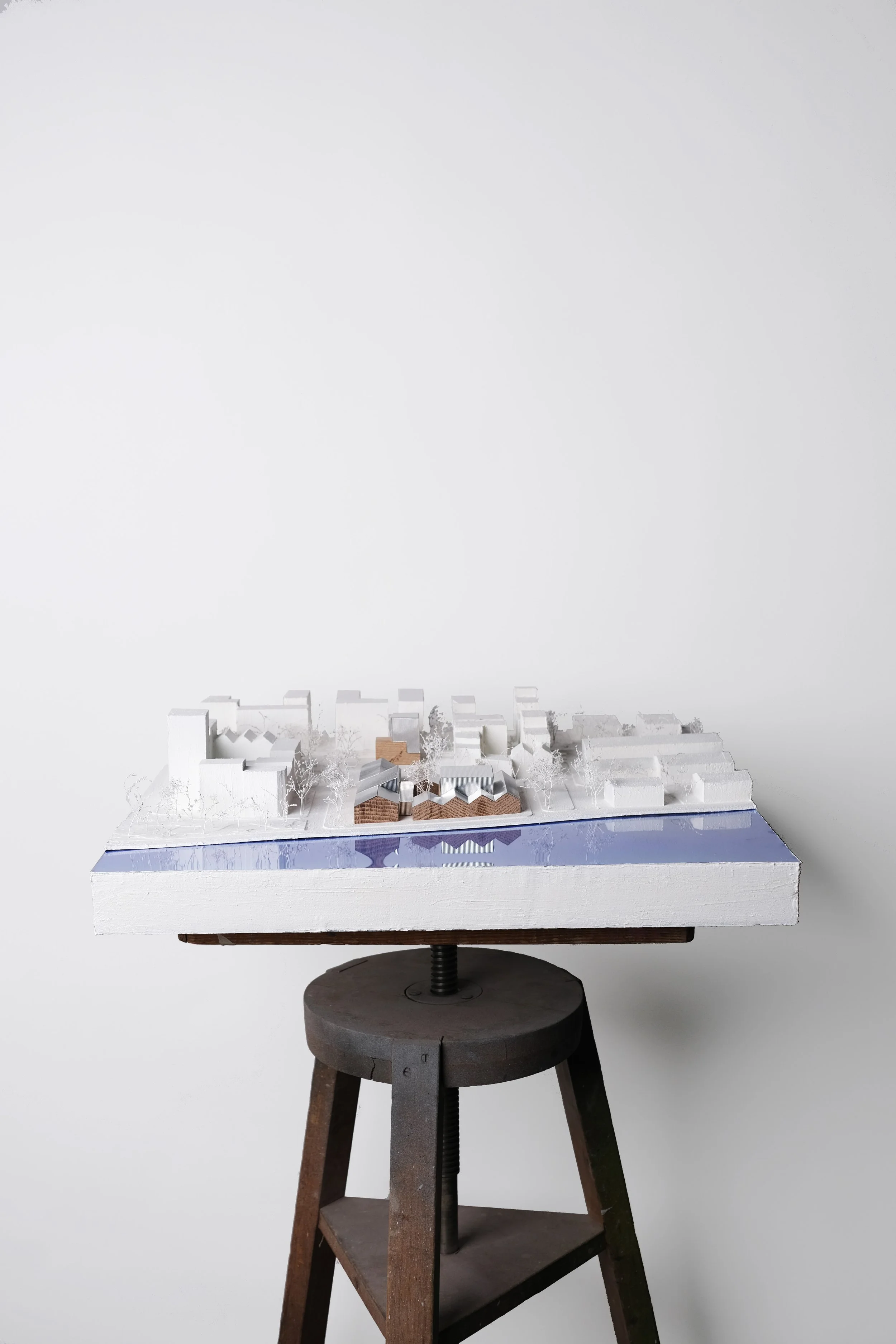 A detailed architectural model of a modern residential development with multiple buildings, trees, and a water feature, set on a white base and displayed on a black stand.