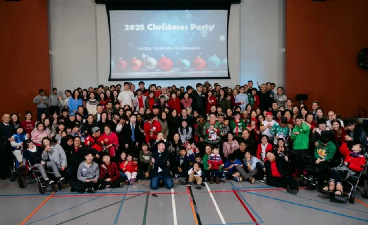 A large group of people, including children and adults, gathered in a gymnasium for a Christmas party in 2025, with a projector screen displaying "2025 Christmas Party" in the background.