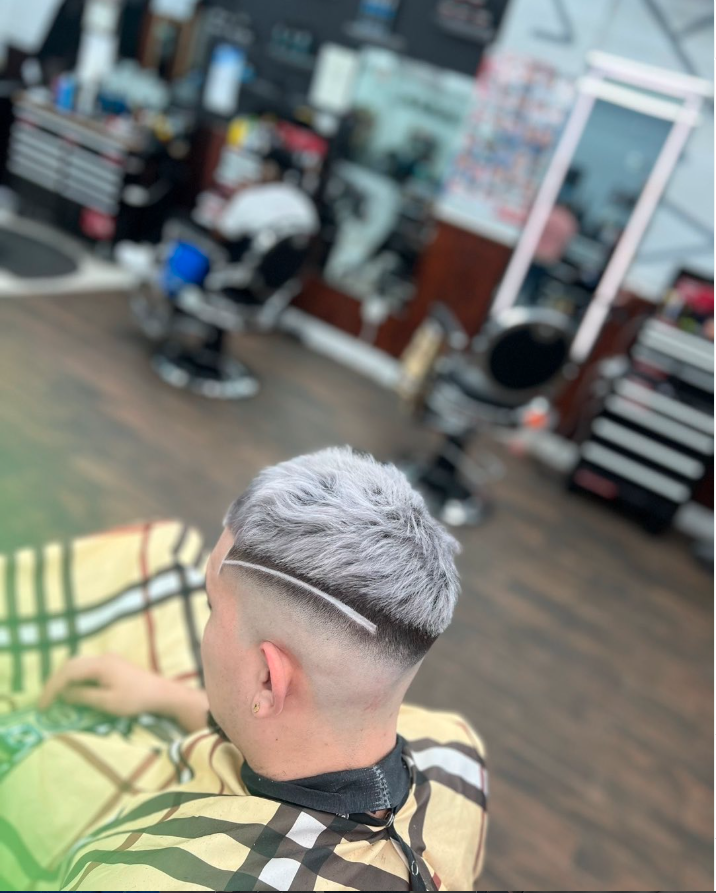 A person with a fresh, trendy two-tone haircut featuring a shaved undercut and a hairline design, sitting in a barber shop.