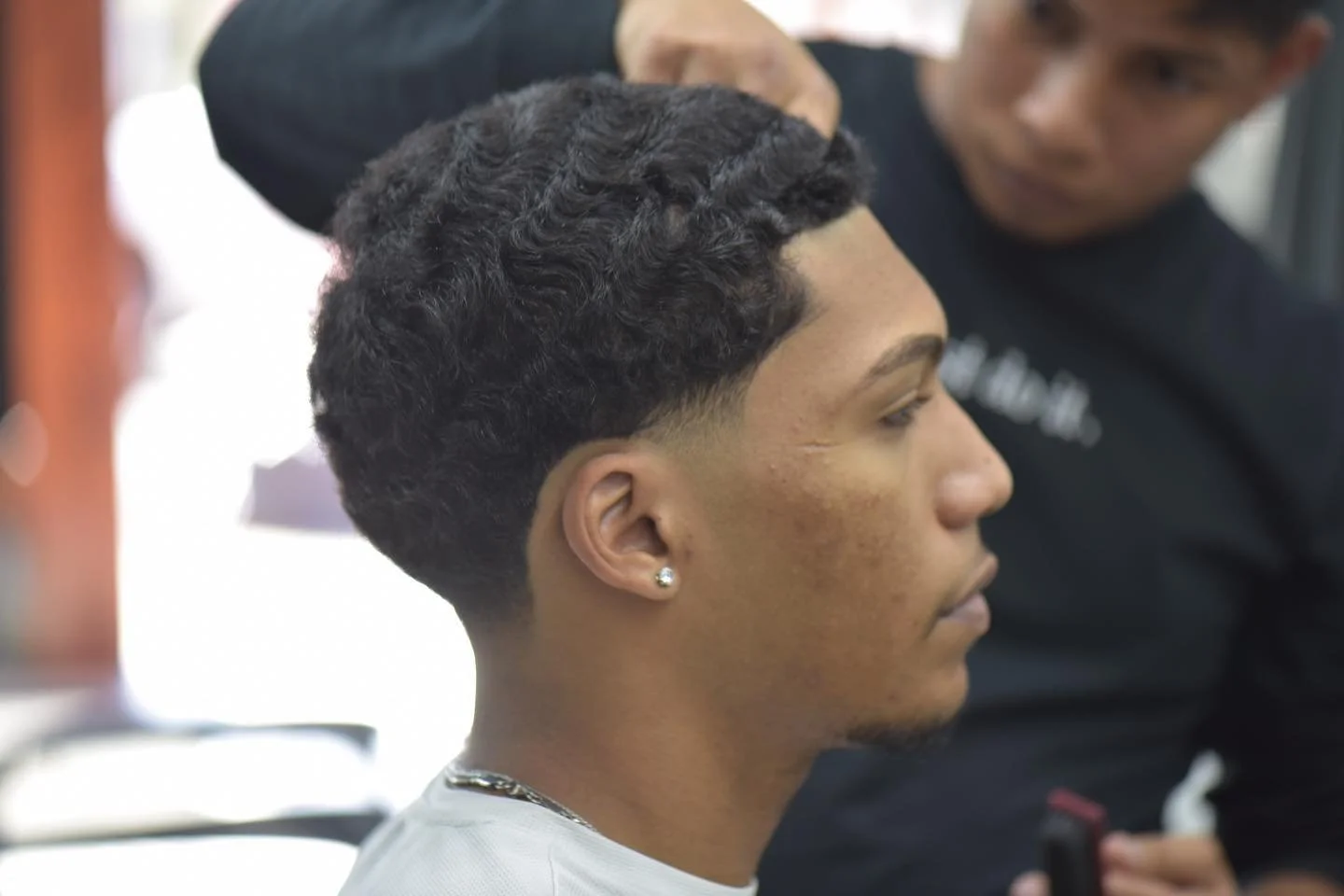 Young man getting a fresh haircut with a fade and textured curls at a barber shop.