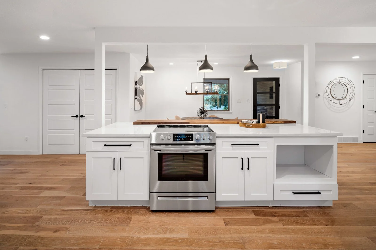 Modern kitchen with white cabinets, a stainless steel oven, and wood flooring. Open layout with a dining area and modern decor.