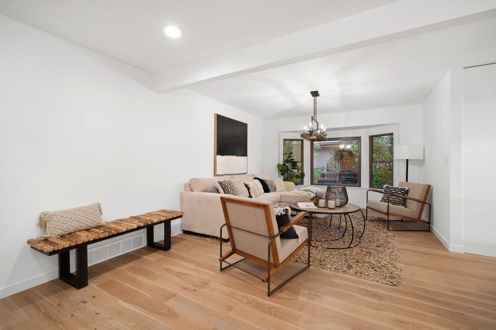 Living room with beige couch, armchairs, round coffee table, large window, wooden flooring, and modern decor.