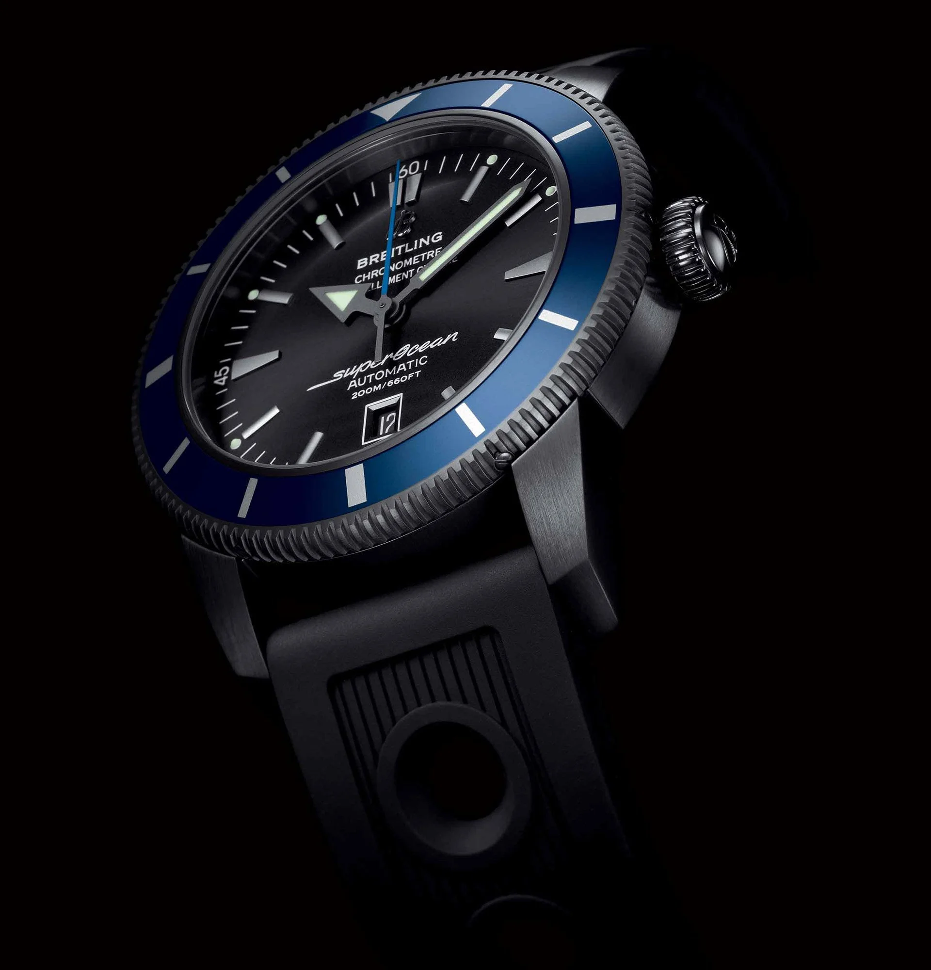 Close-up of a Breitling Superocean wristwatch with a black dial, blue bezel, and black rubber strap on a dark background.